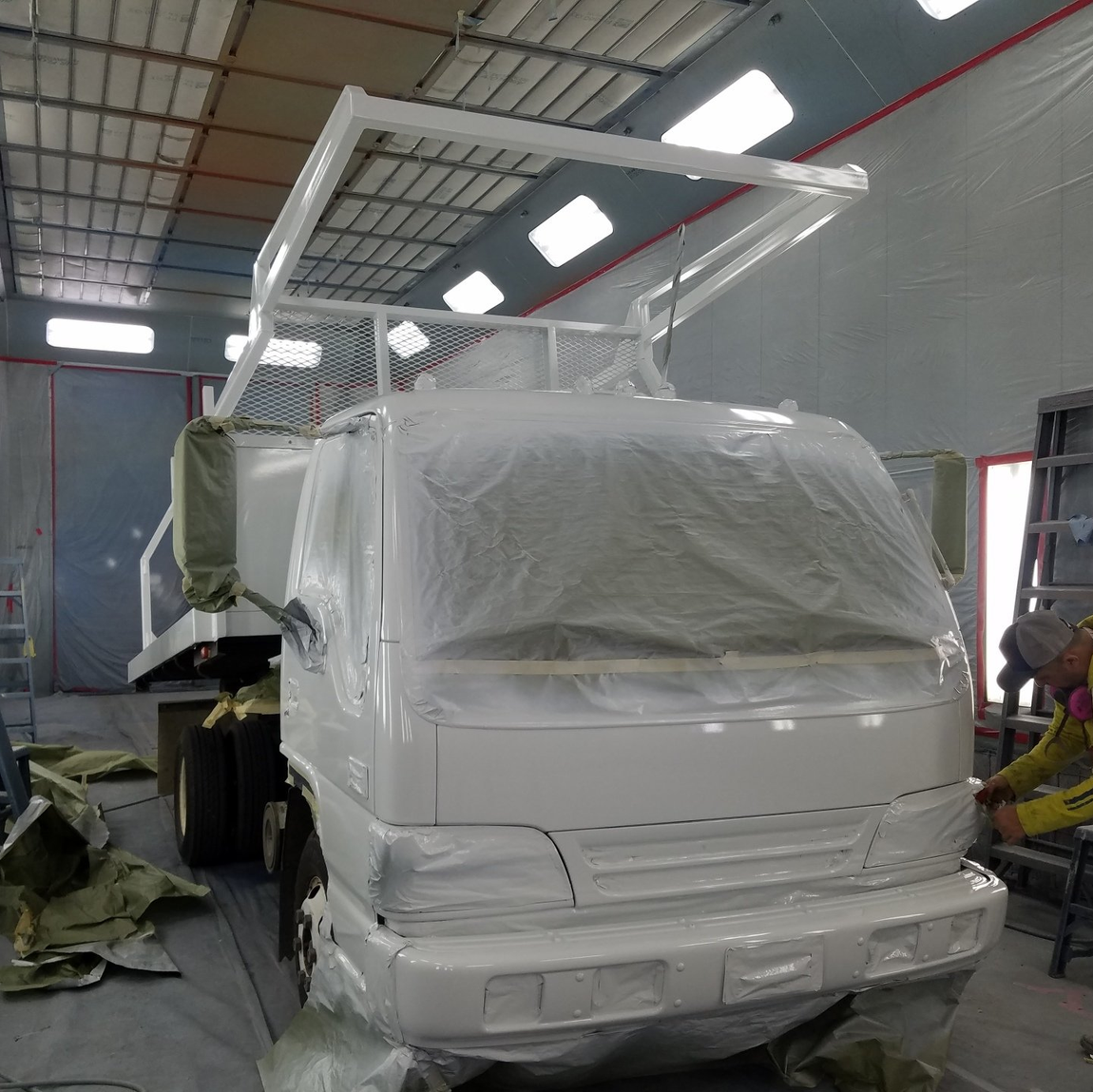 Truck in a warehouse, covered in protective plastic wrap, with a white overhead frame.