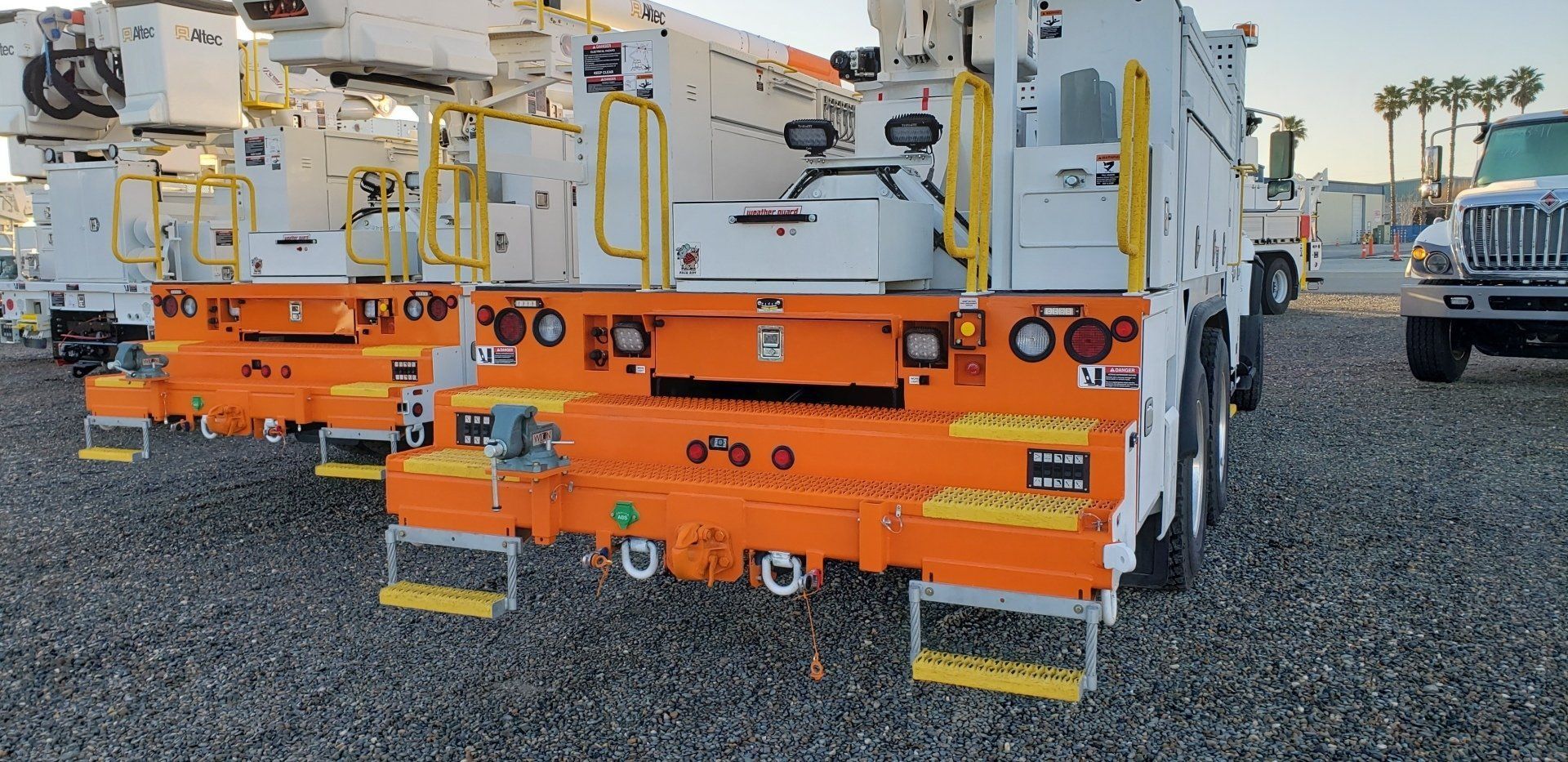Orange heavy-duty tow truck rear view on a gravel lot, with hydraulic equipment and white boom arms