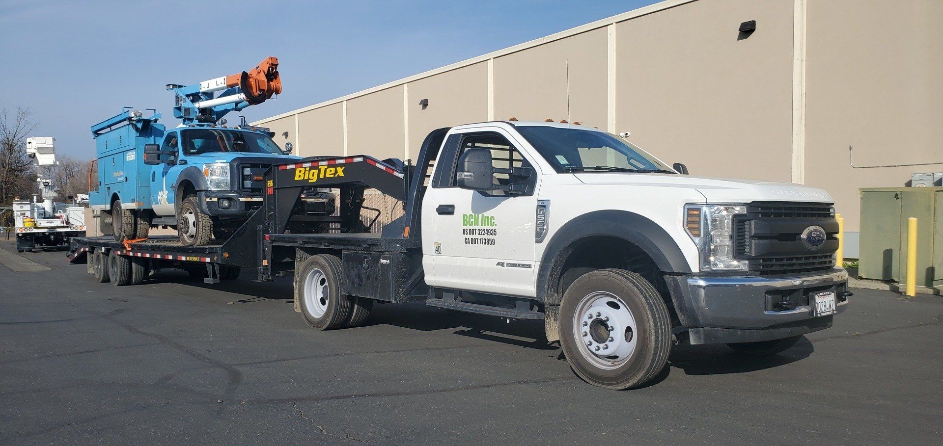 White utility truck with mounted equipment trailer parked beside a beige building outdoors