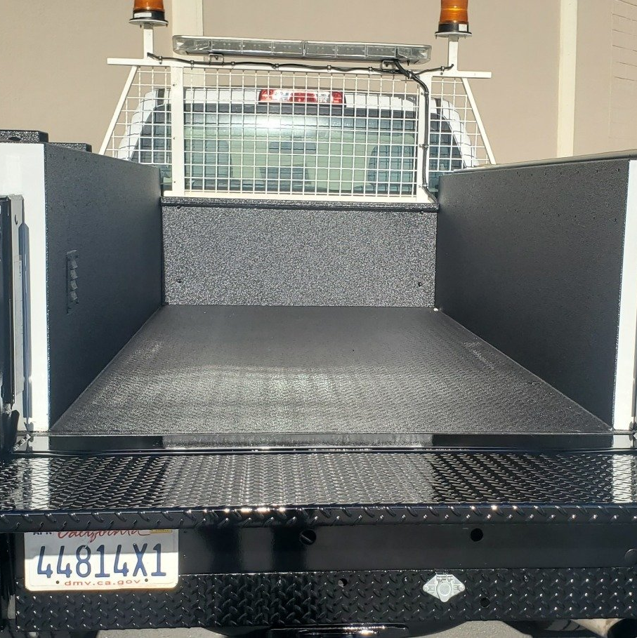 Black flatbed truck bed with mesh cab guard, side rails, and amber warning lights; front license plate visible