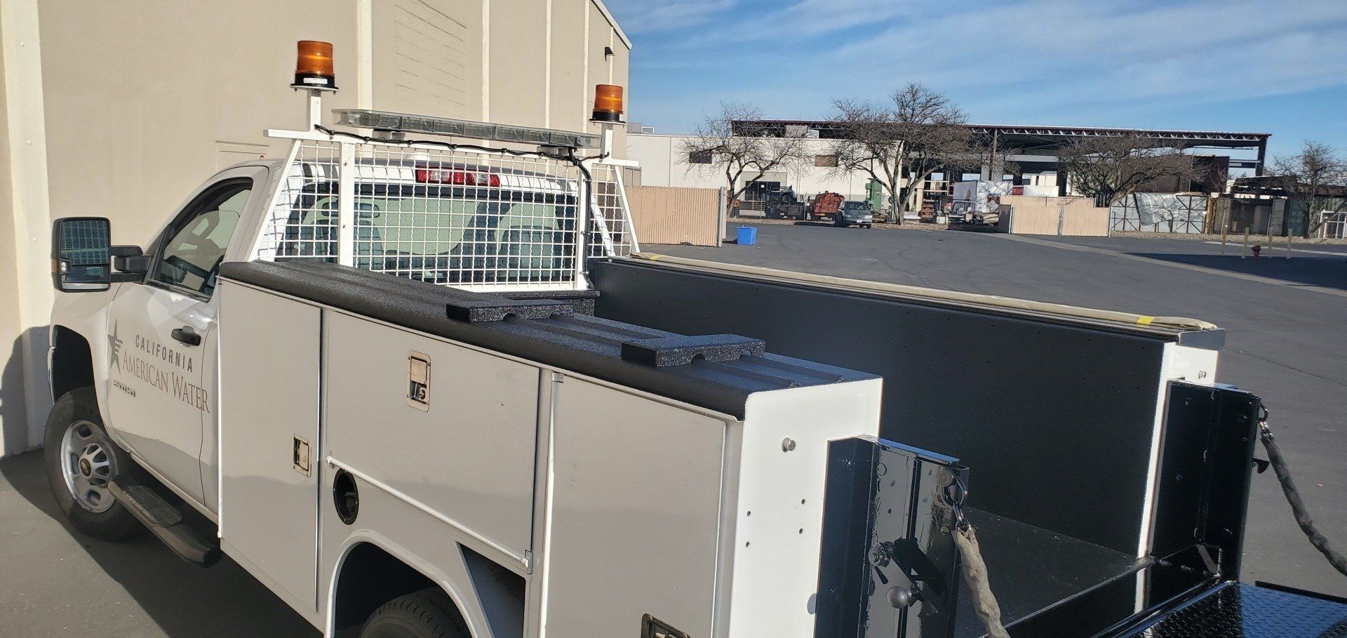 White utility truck with flatbed and amber beacon parked outdoors near a building.