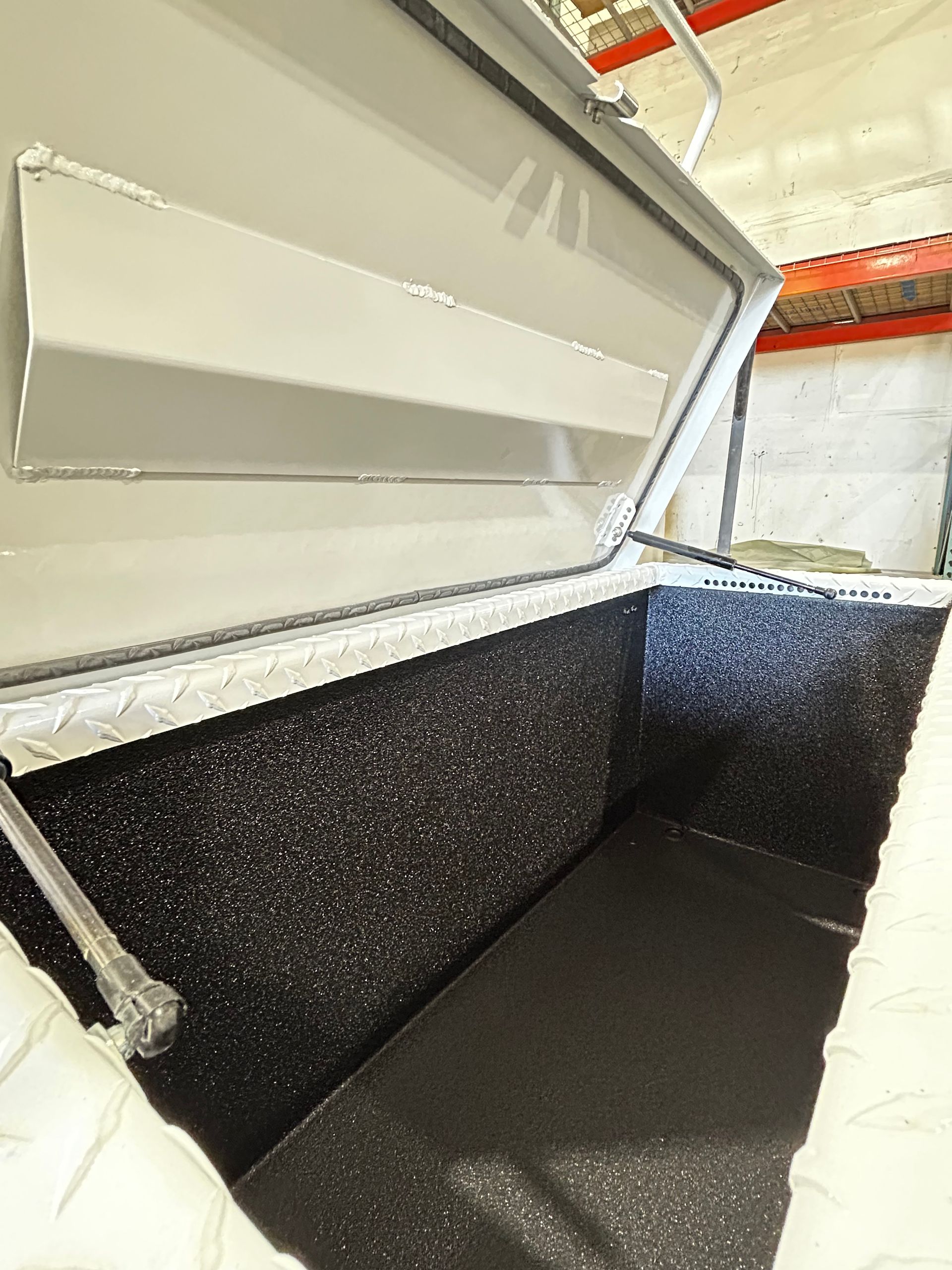 Open insulated chest freezer with black interior and white lid in a warehouse.