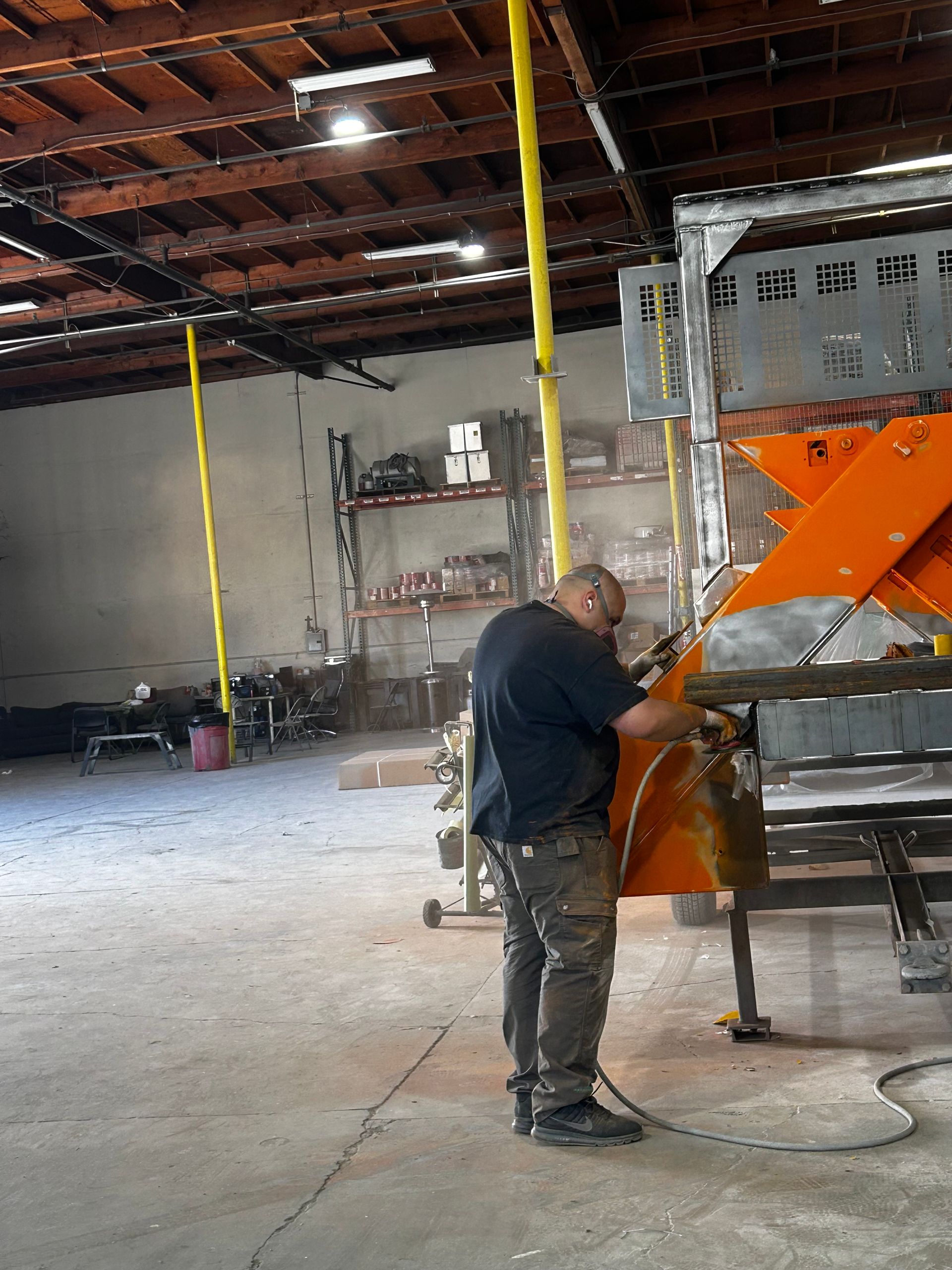 Man working with an orange machine in a large warehouse with exposed ceiling beams.