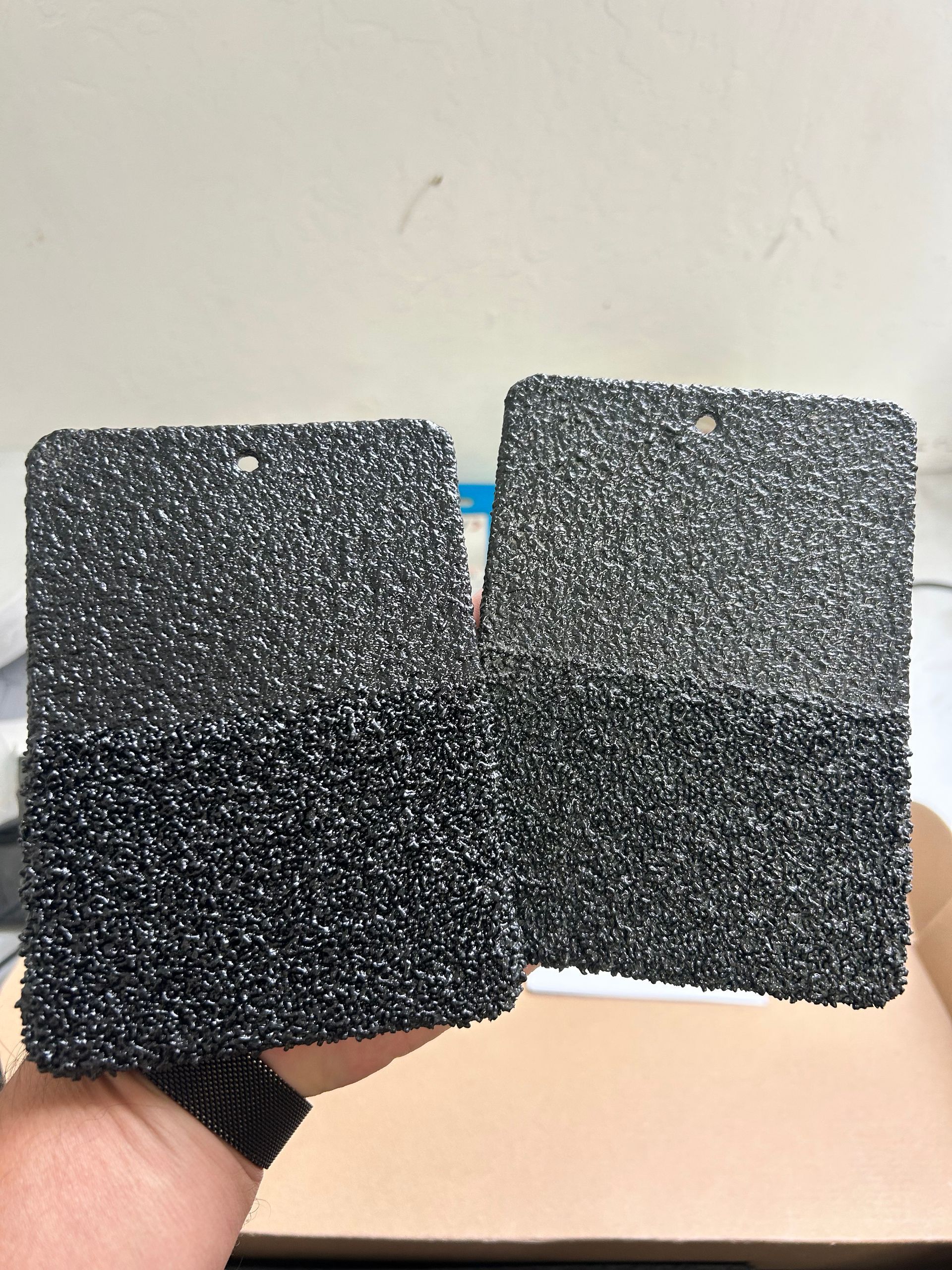 Two black textured square foam pads held side by side against a white wall