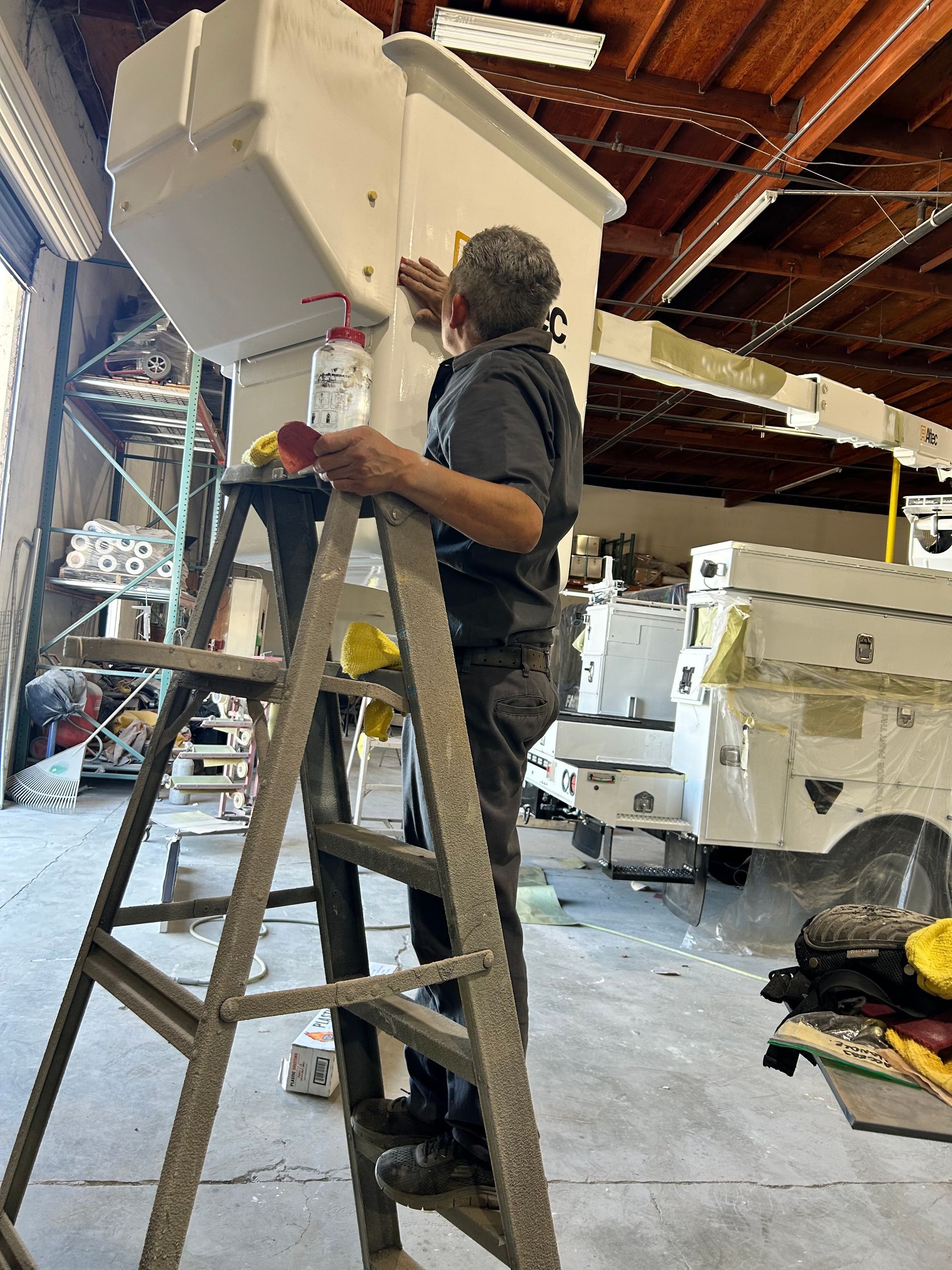 Person on a ladder painting a white ceiling beam in a workshop garage