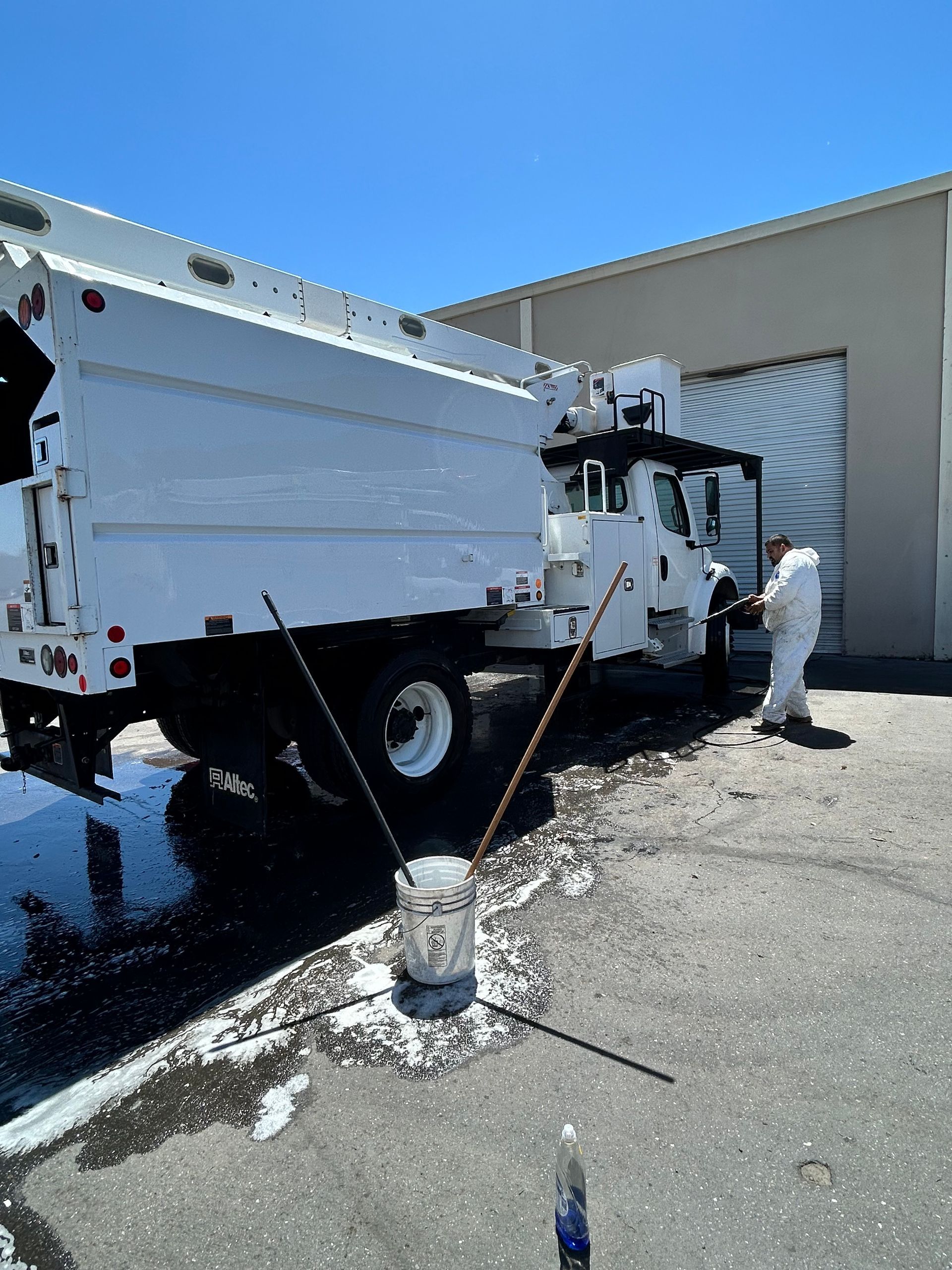 White utility truck with a worker beside it, parked on gravel outside a building under a blue sky.