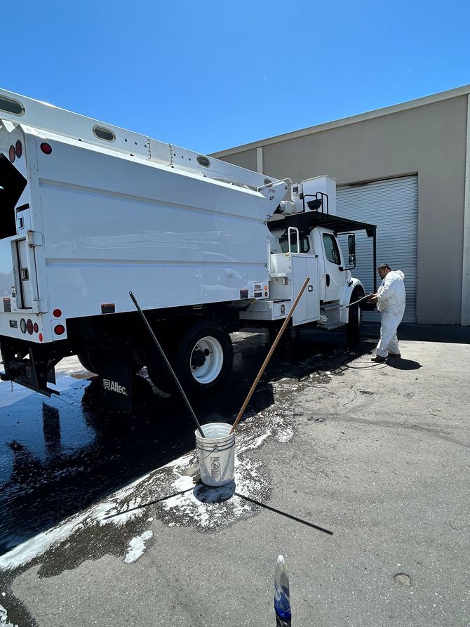 White utility truck parked beside a building, with a worker standing nearby on a sunny gravel lot.