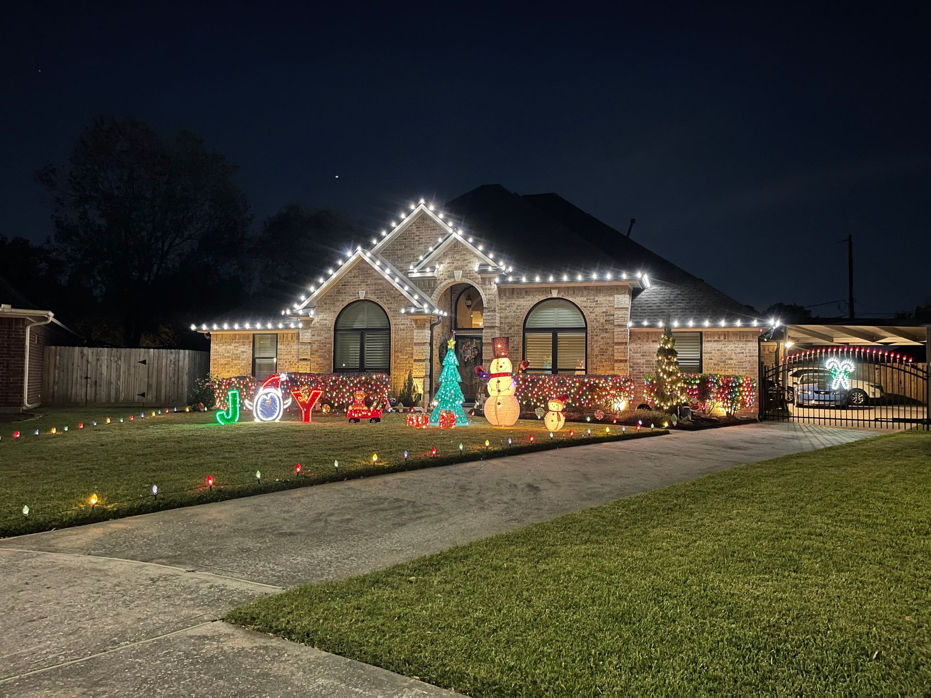 House decorated for Christmas with white roof lights, lawn displays, and colorful lights along the walkway.