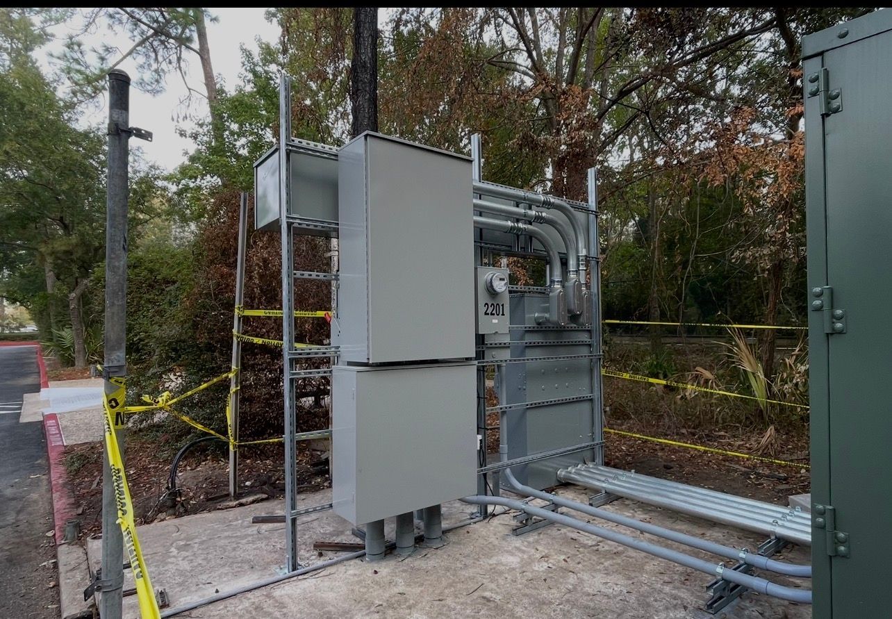 Gray electrical boxes and conduit outside, next to trees. Yellow caution tape in foreground.