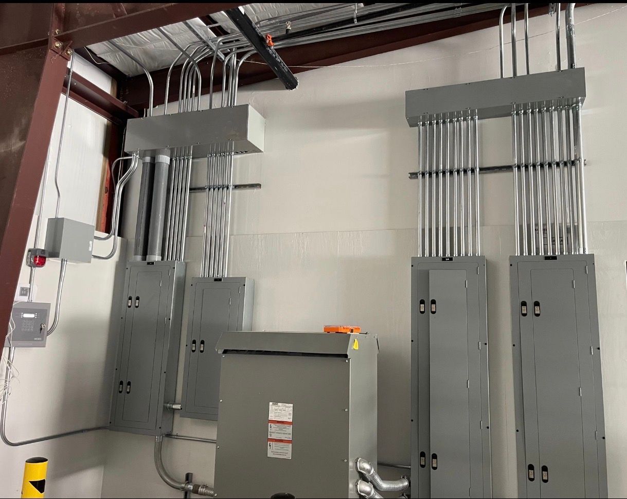 Electrical panel room with gray cabinets, conduit pipes, and exposed ceiling beams