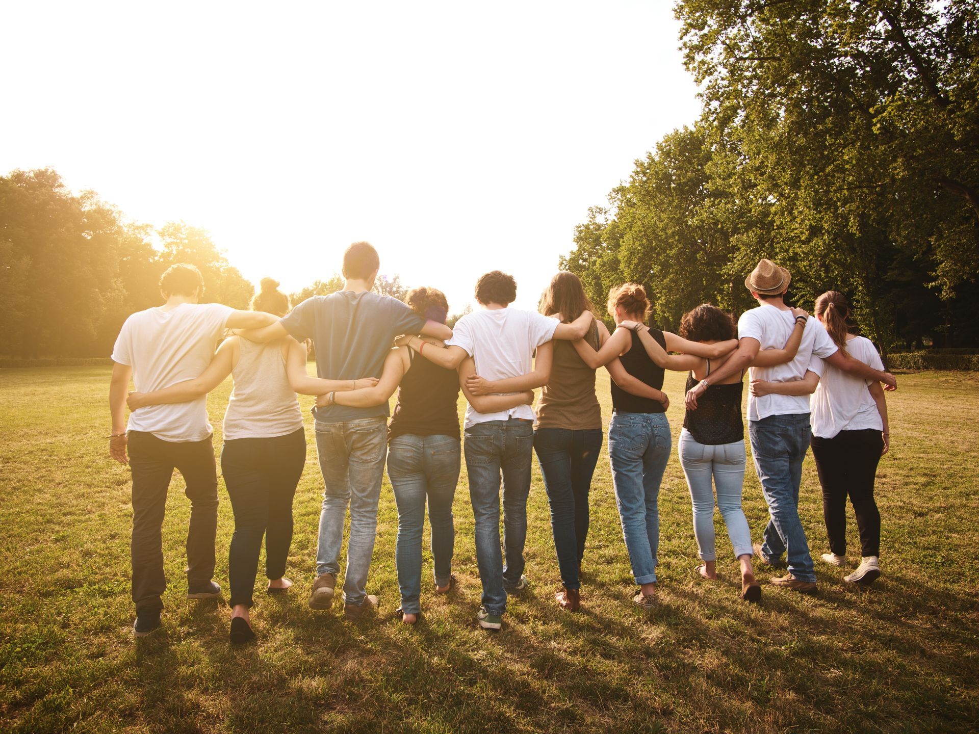 Group of people standing arm-in-arm in a sunlit park at sunset
