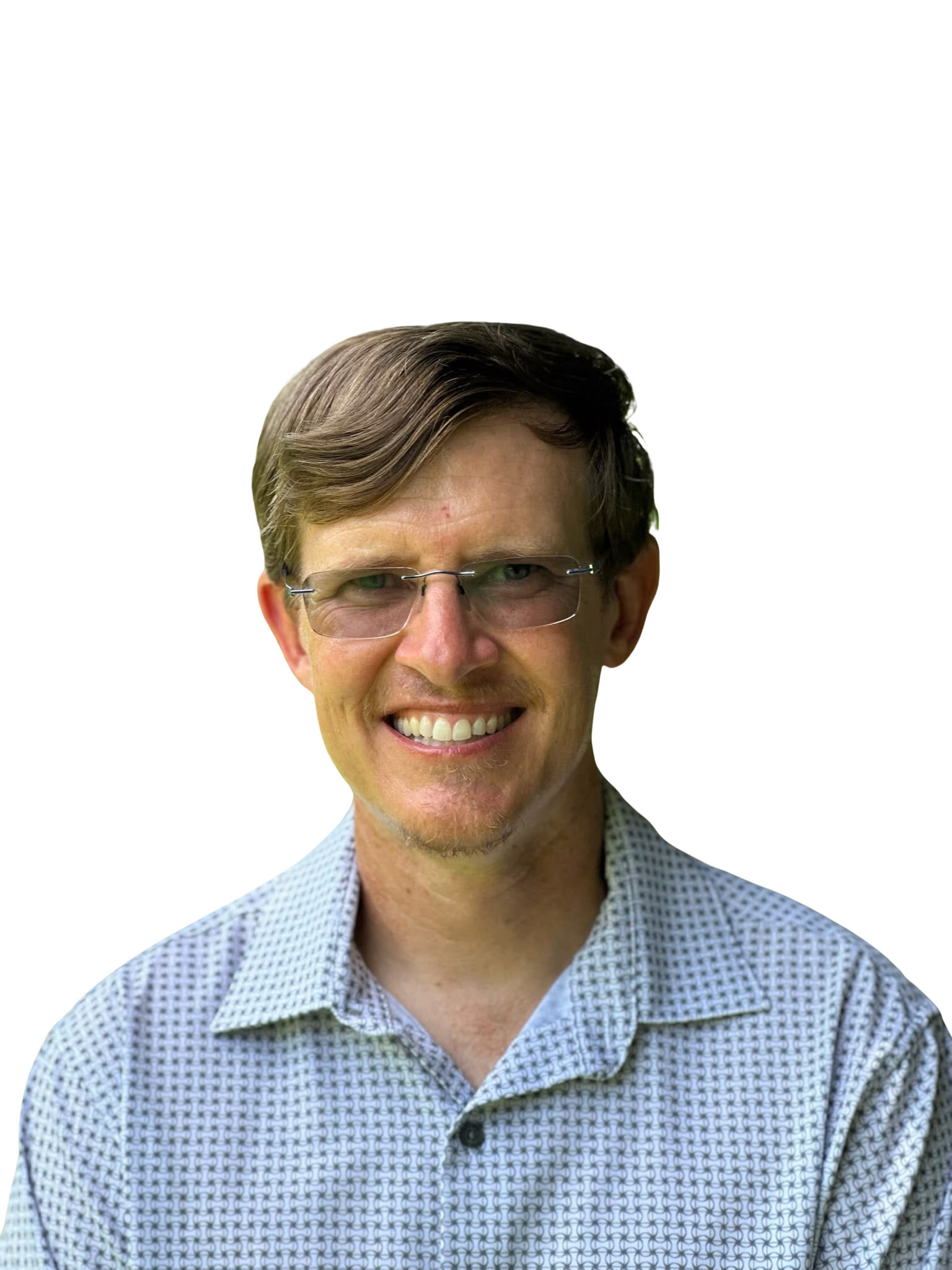 Smiling person wearing glasses and a light blue shirt outdoors with green trees in the background