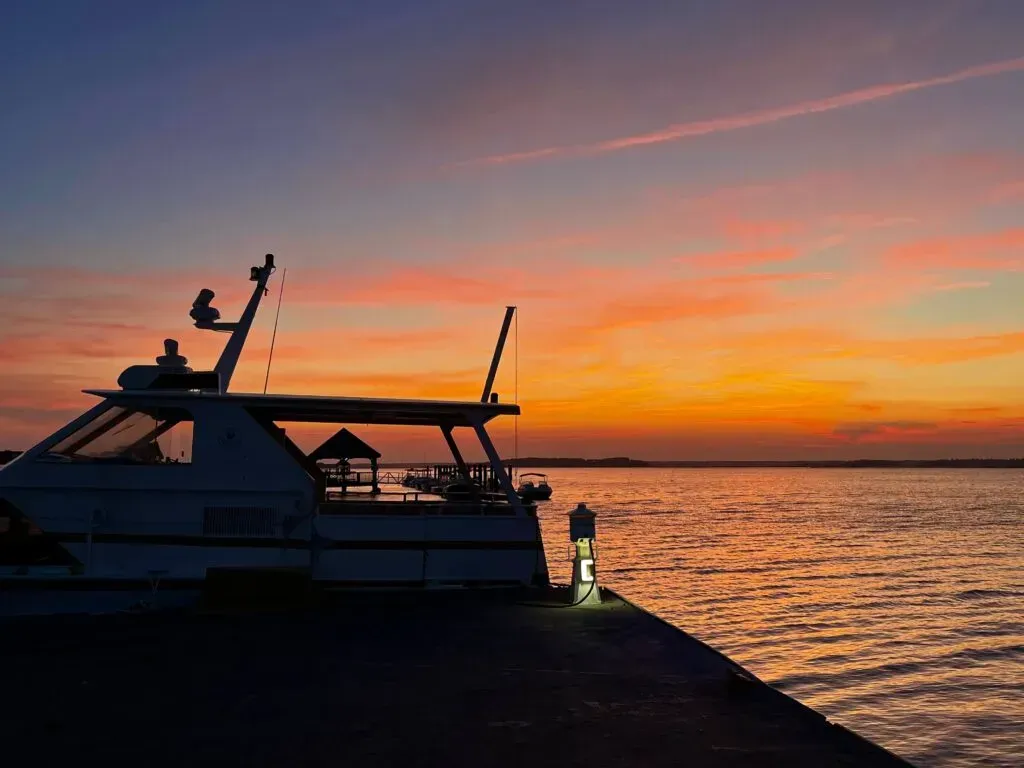 Boat silhouetted against a colorful sunset over a calm body of water.