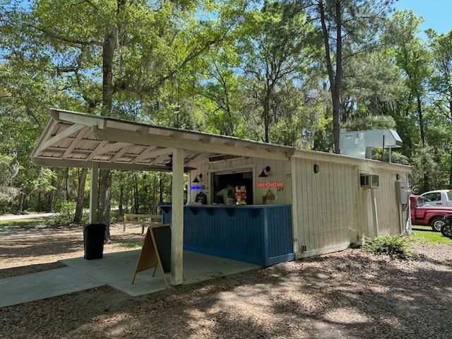 Small white bar with blue accents, under a canopy, in a wooded area. An open sign is visible.