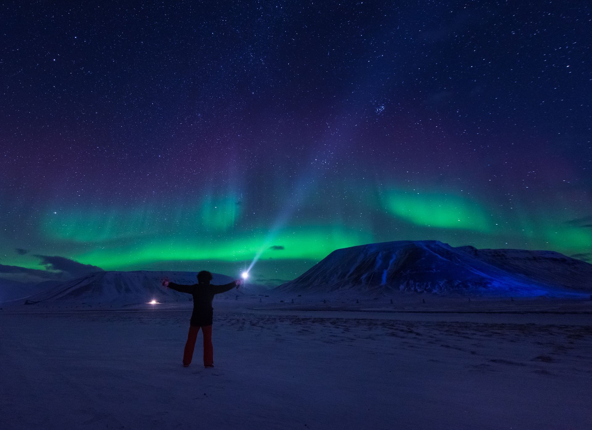 A person is standing in the snow looking at the aurora borealis.