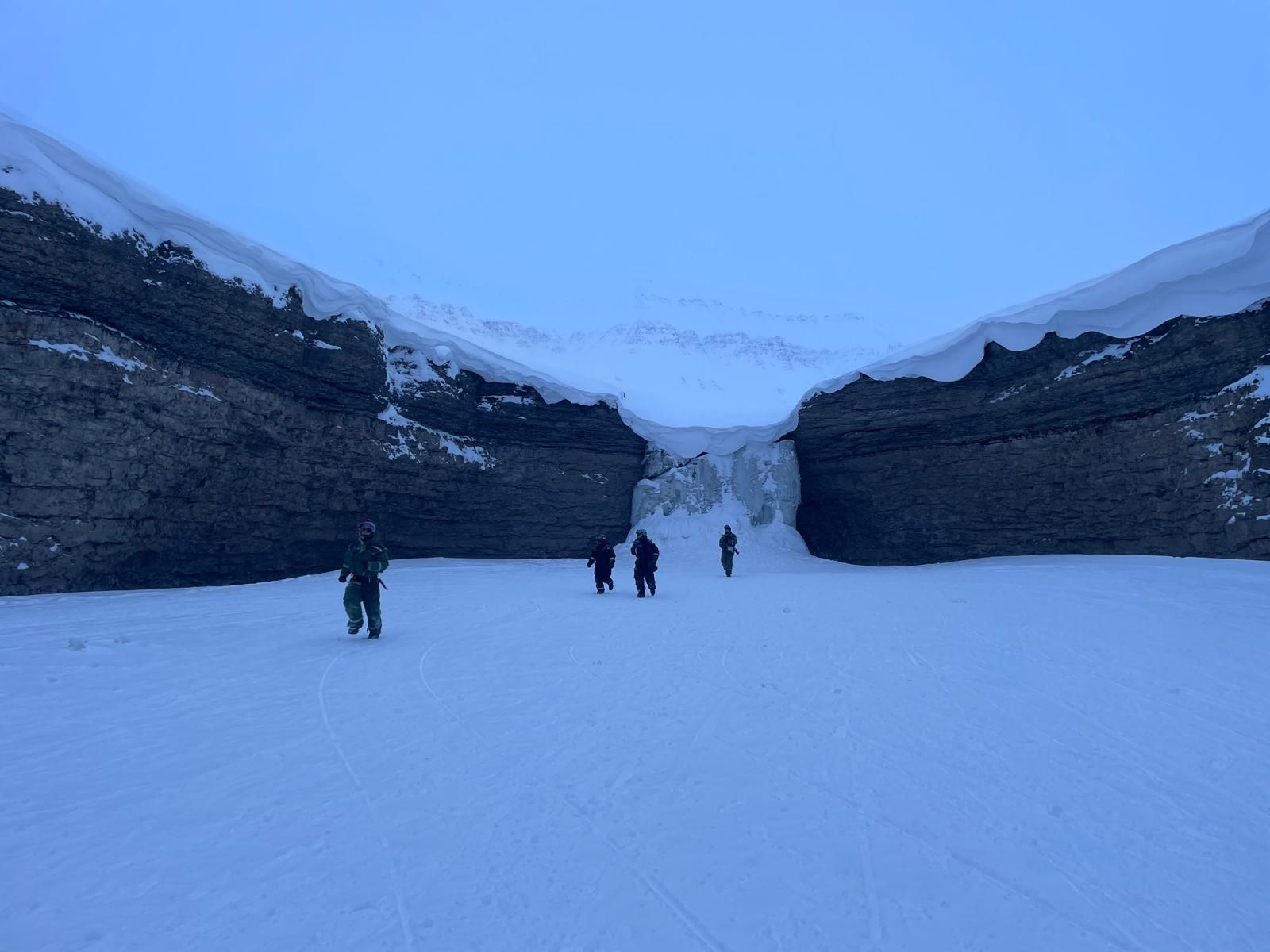A group of people are walking through the snow in the mountains.