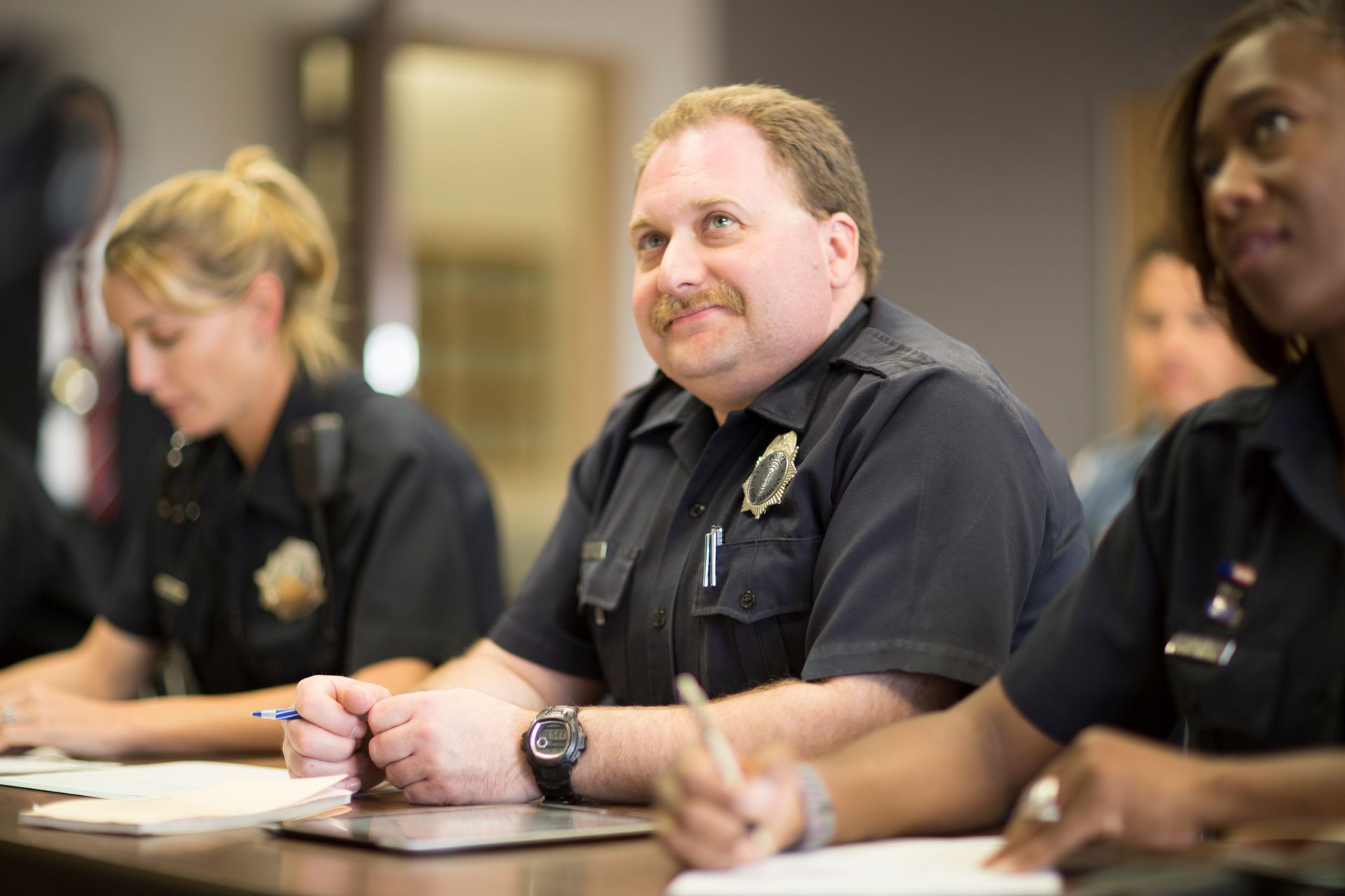 Uniformed officers seated at a table taking notes during a law enforcement training session. Uniformed officers seated at a table taking notes during a law enforcement training session.
