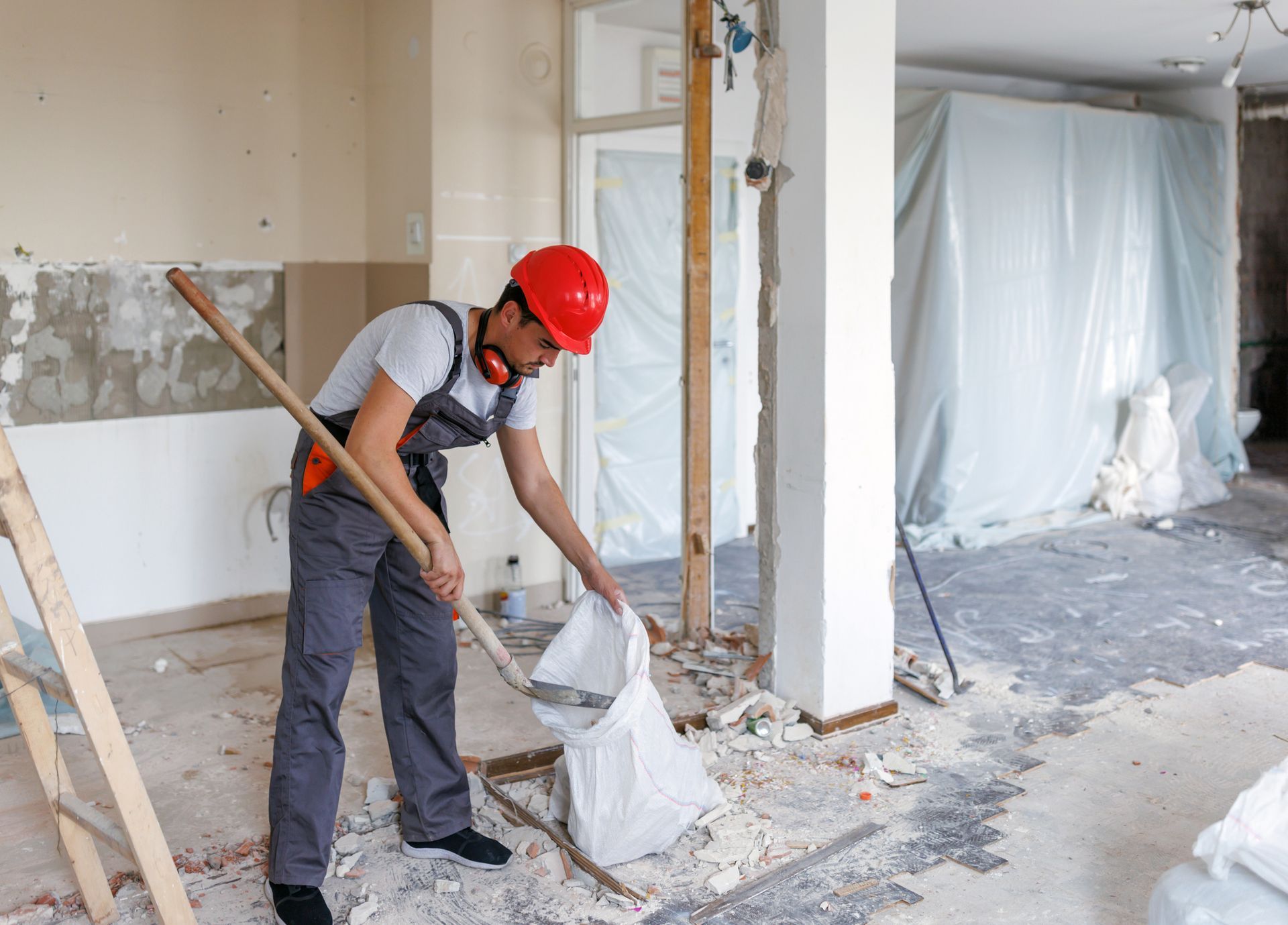 A construction worker is holding a shovel and a bag of cement.