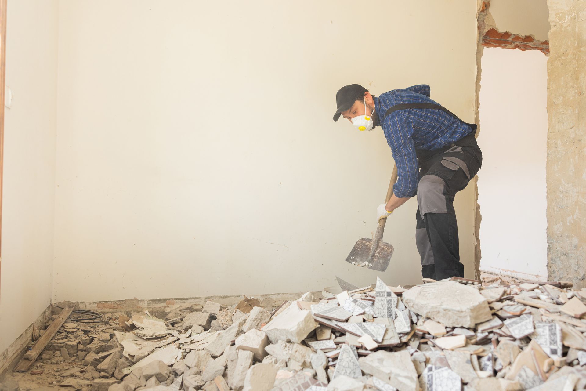 A man wearing a mask and a shovel is demolishing a wall.
