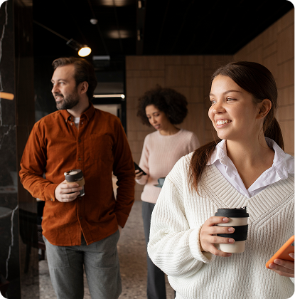Three coworkers walking and chatting in a hallway, each holding a coffee cup.