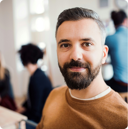 Portrait of a smiling man in a brown sweater in a blurred indoor office setting