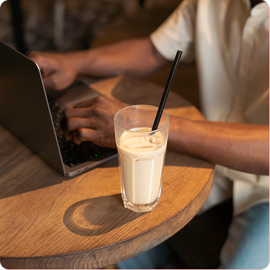 Laptop and iced drink on a wooden table beside a person typing indoors