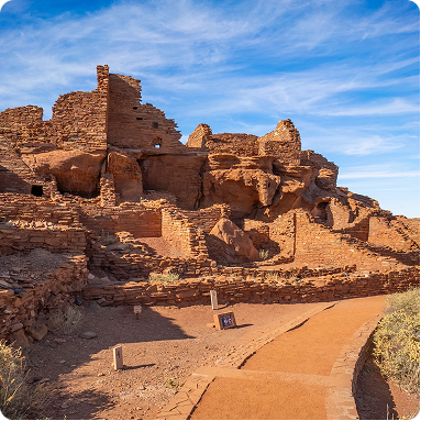 Ancient desert ruins of stone walls and buildings under a blue sky.