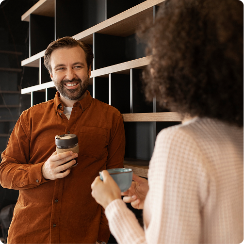Two people chatting in a modern office, each holding a takeaway coffee cup.