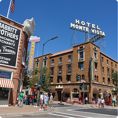 Street scene with Hotel Monte Vista sign, brick buildings, and pedestrians at a sunny intersection.
