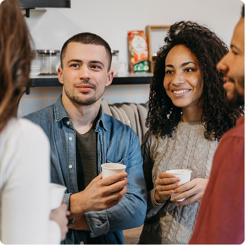Four people chatting and smiling while holding coffee cups in a casual indoor setting