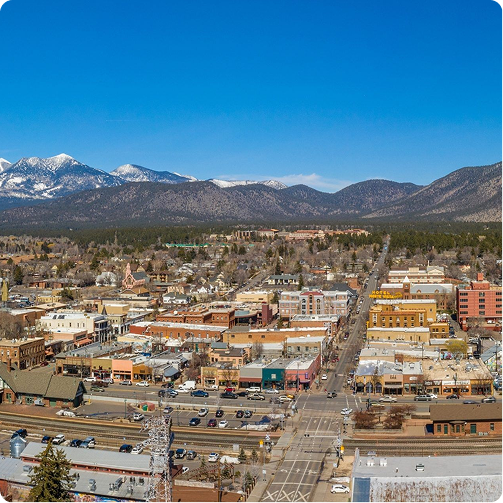 Downtown mountain town beneath snowy peaks and blue sky, with streets and buildings in the foreground