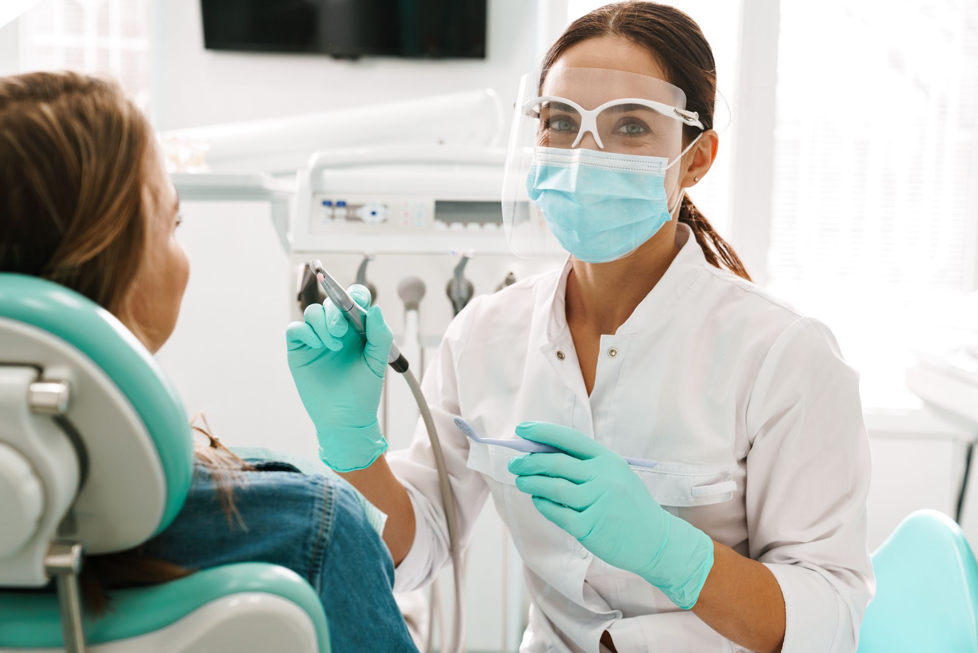 Dental professional wearing protective gear treating a patient in a dental clinic chair. Dental professional wearing protective gear treating a patient in a dental clinic chair.