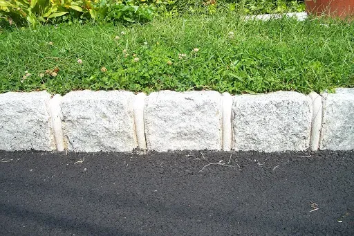 Yellow painted concrete curb next to asphalt road. Green shrubs in background.