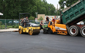 Construction workers paving asphalt with a roller and asphalt paver.