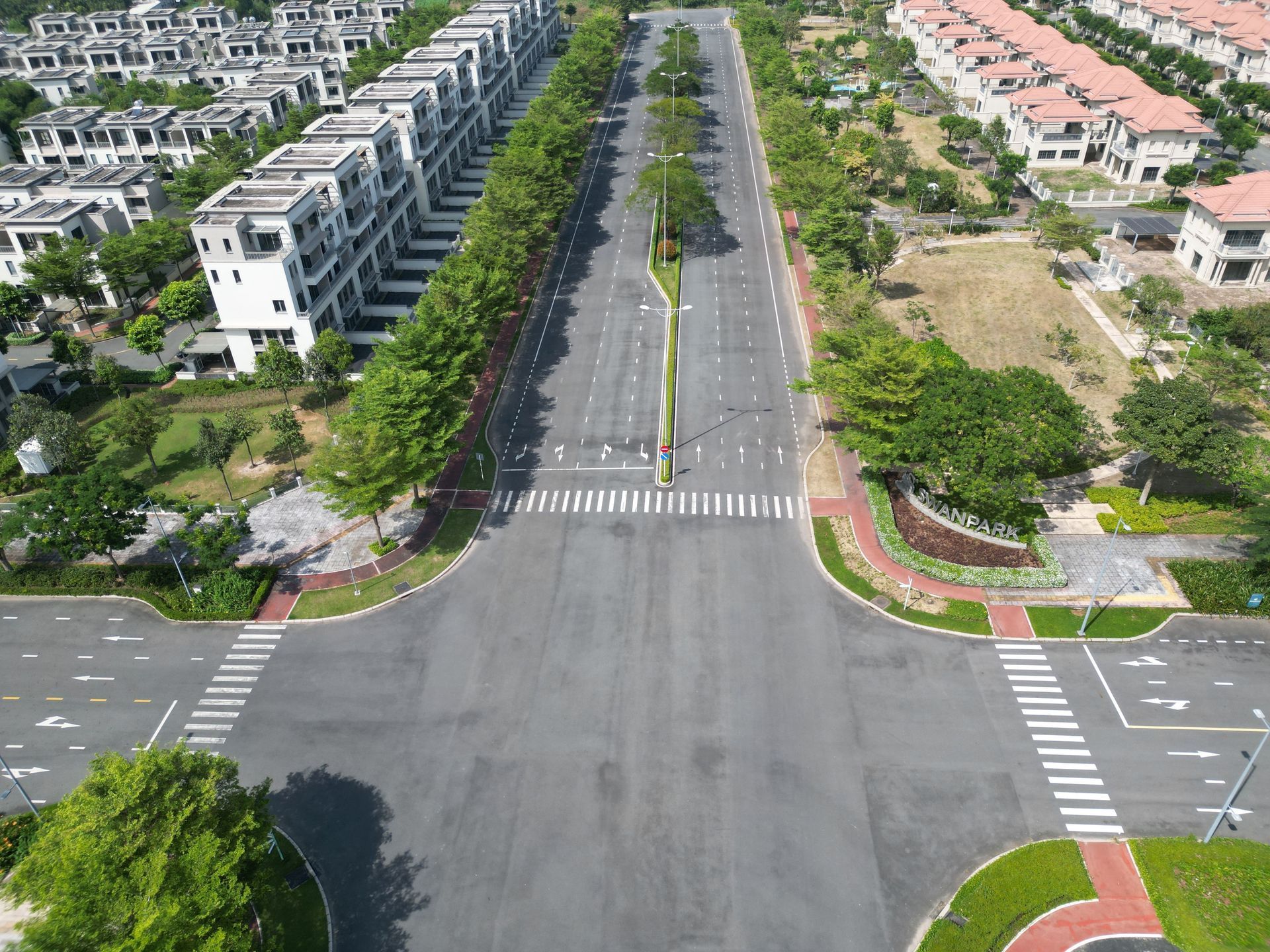 Aerial view of a wide empty boulevard lined with trees and residential buildings at an intersection.