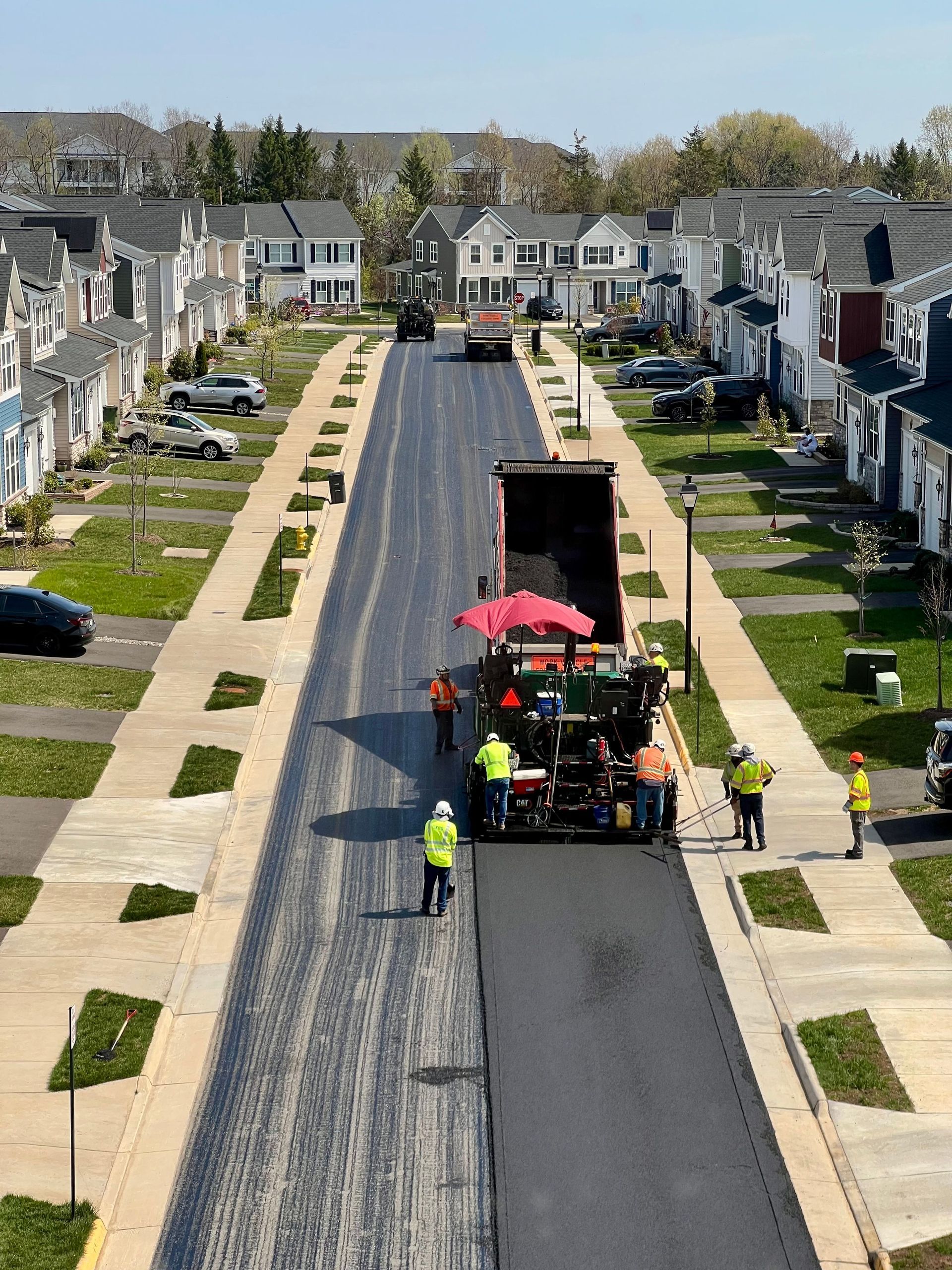 Roadwork crew paving a suburban street with a black asphalt machine and workers in safety vests
