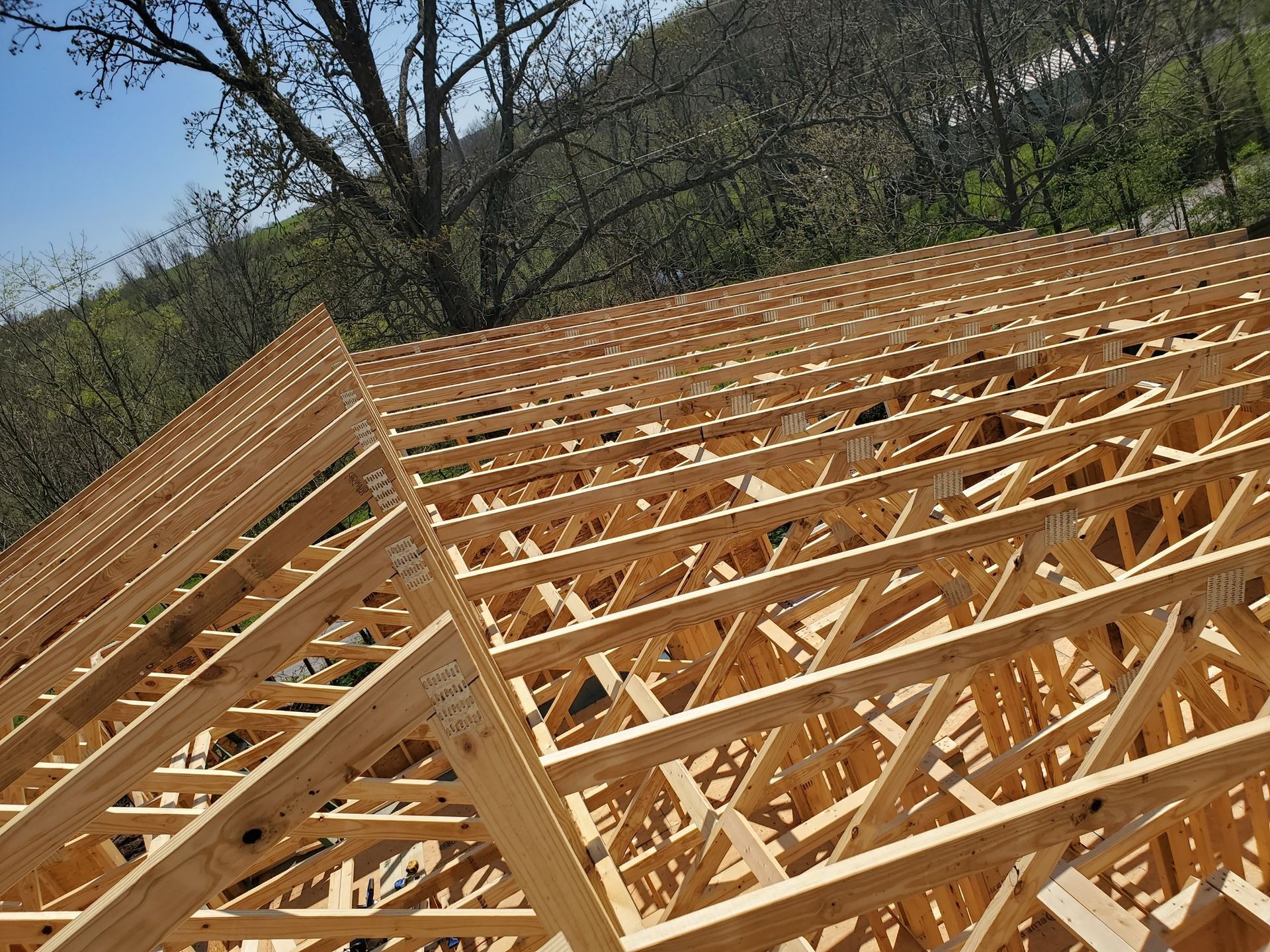 A high-angle view of wooden roof trusses installed on a building under construction against a background of trees.