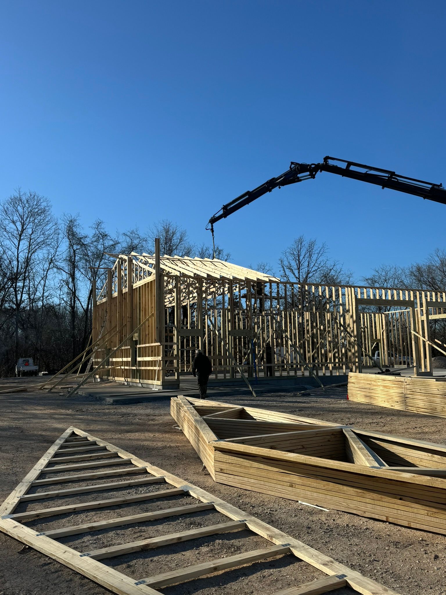 Wood-framed house under construction with a crane arm overhead on a clear blue day