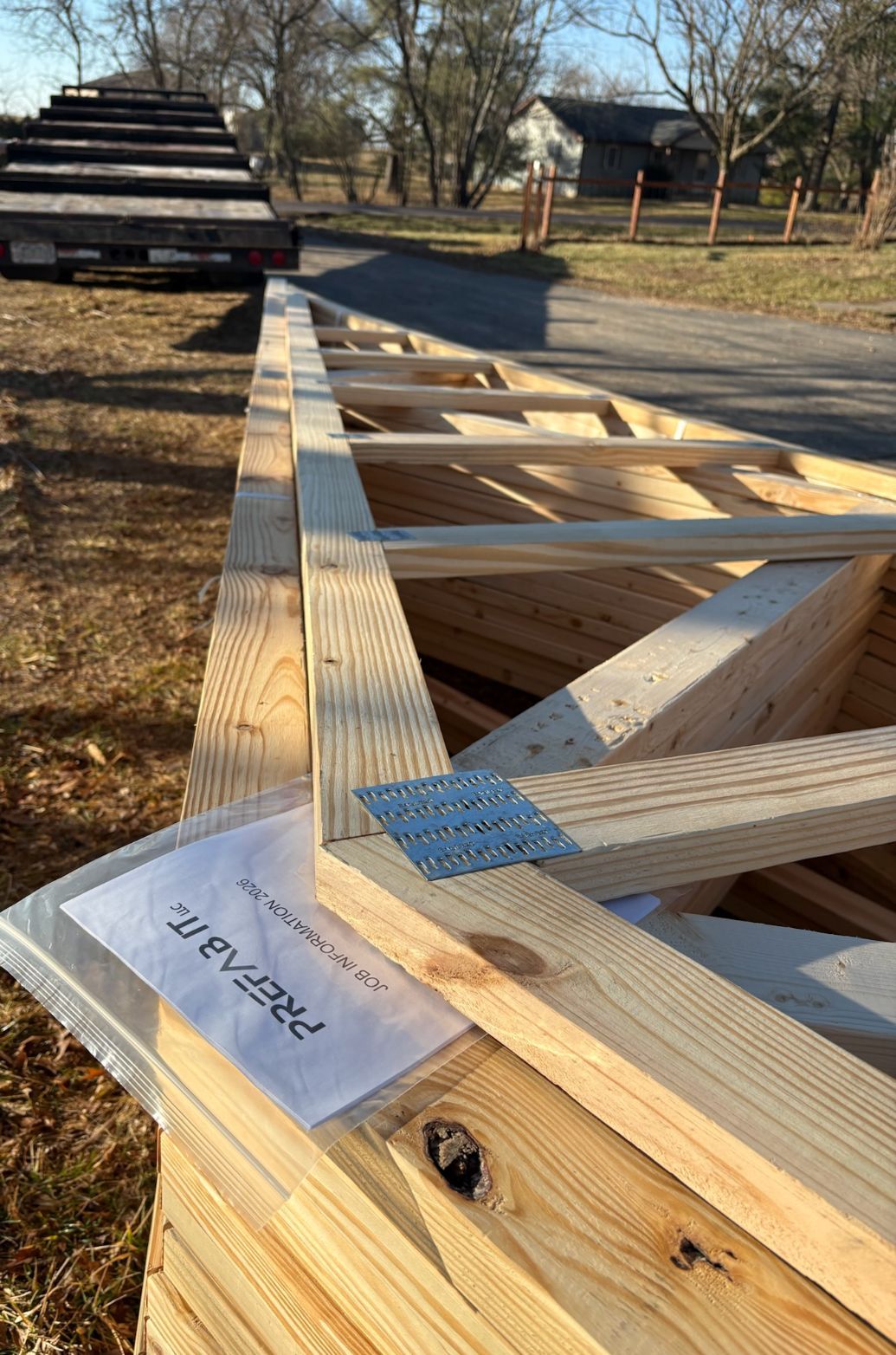 Wooden roof trusses laid out outdoors on a construction site, with a house and trees in the background