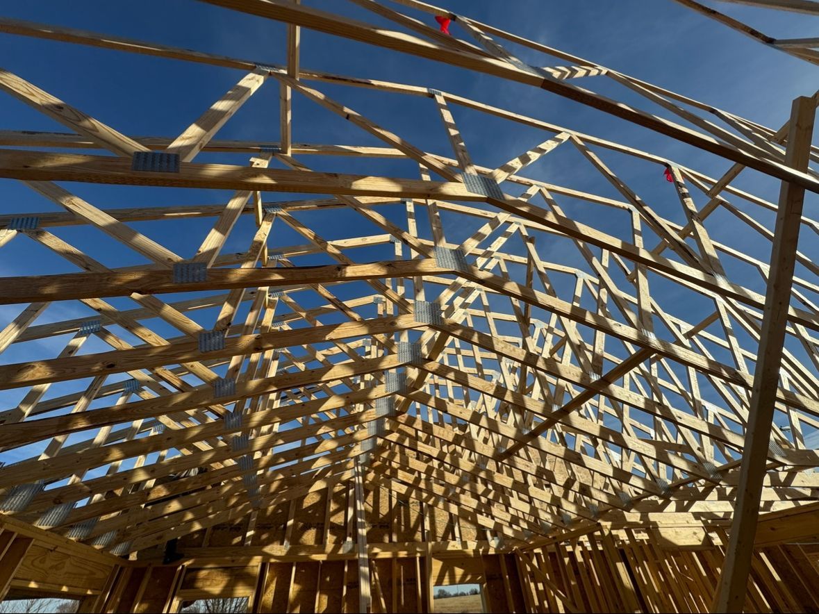 The wooden roof framing of a house under construction against a clear blue sky.