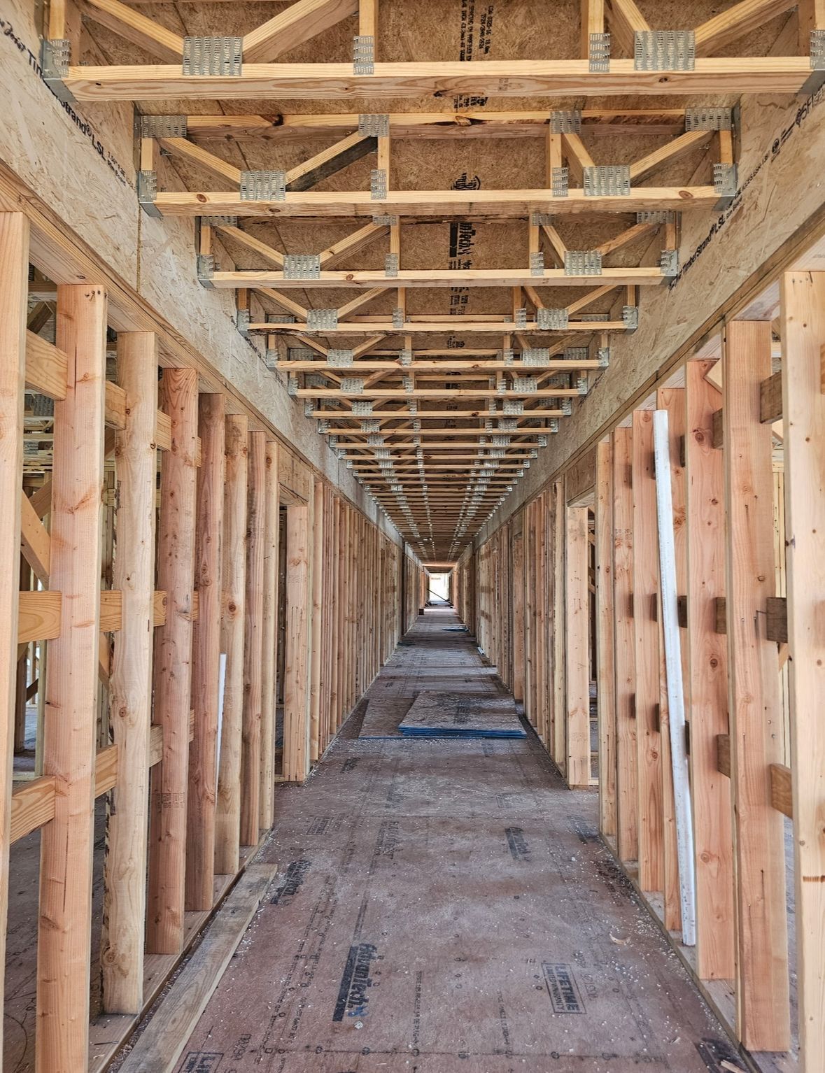 An unfinished wooden building hallway looking down a long, central corridor with exposed floor trusses and wall studs.