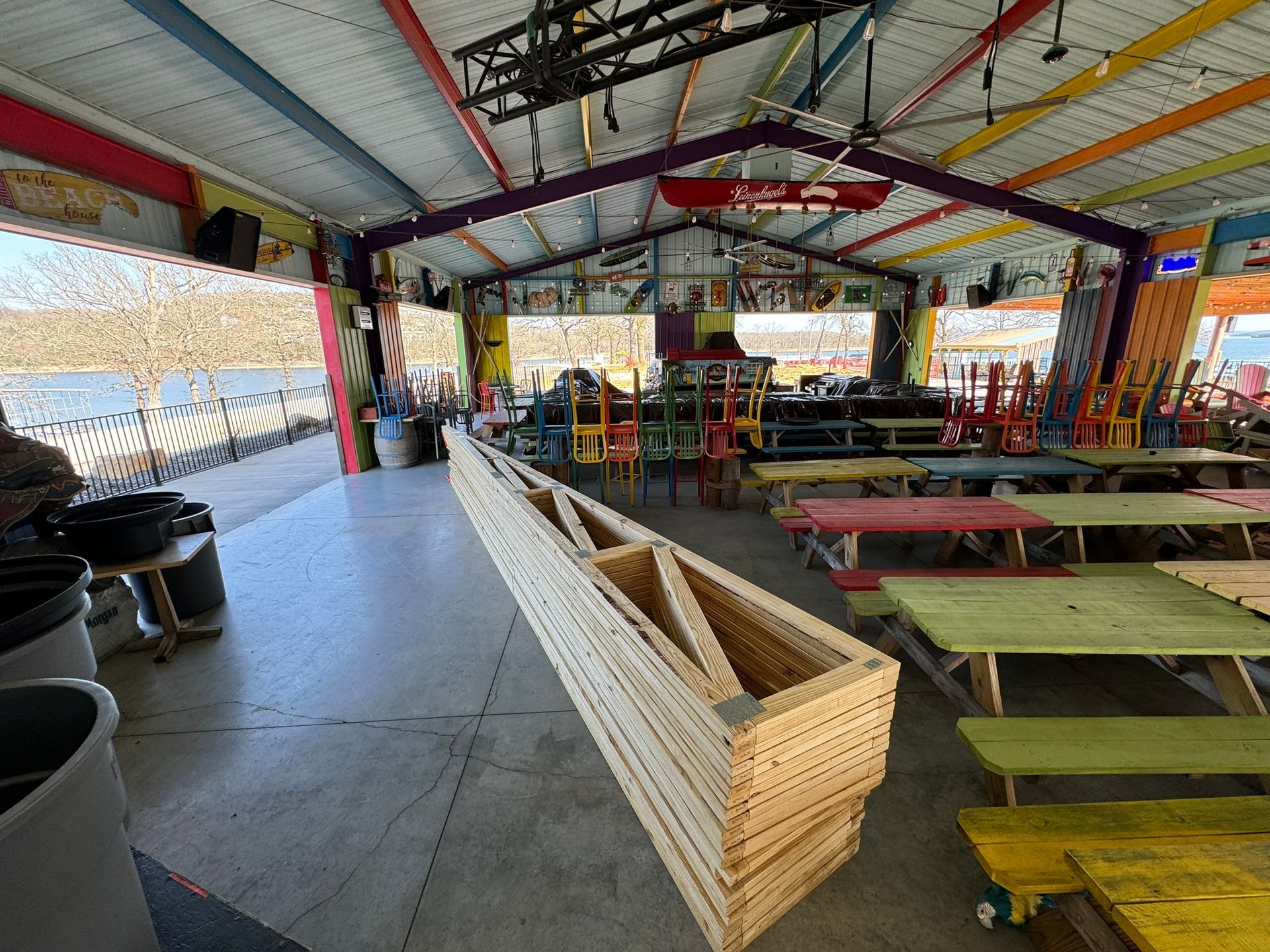 Colorful open-air dining hall with long picnic tables, benches, and a wooden planter in the foreground