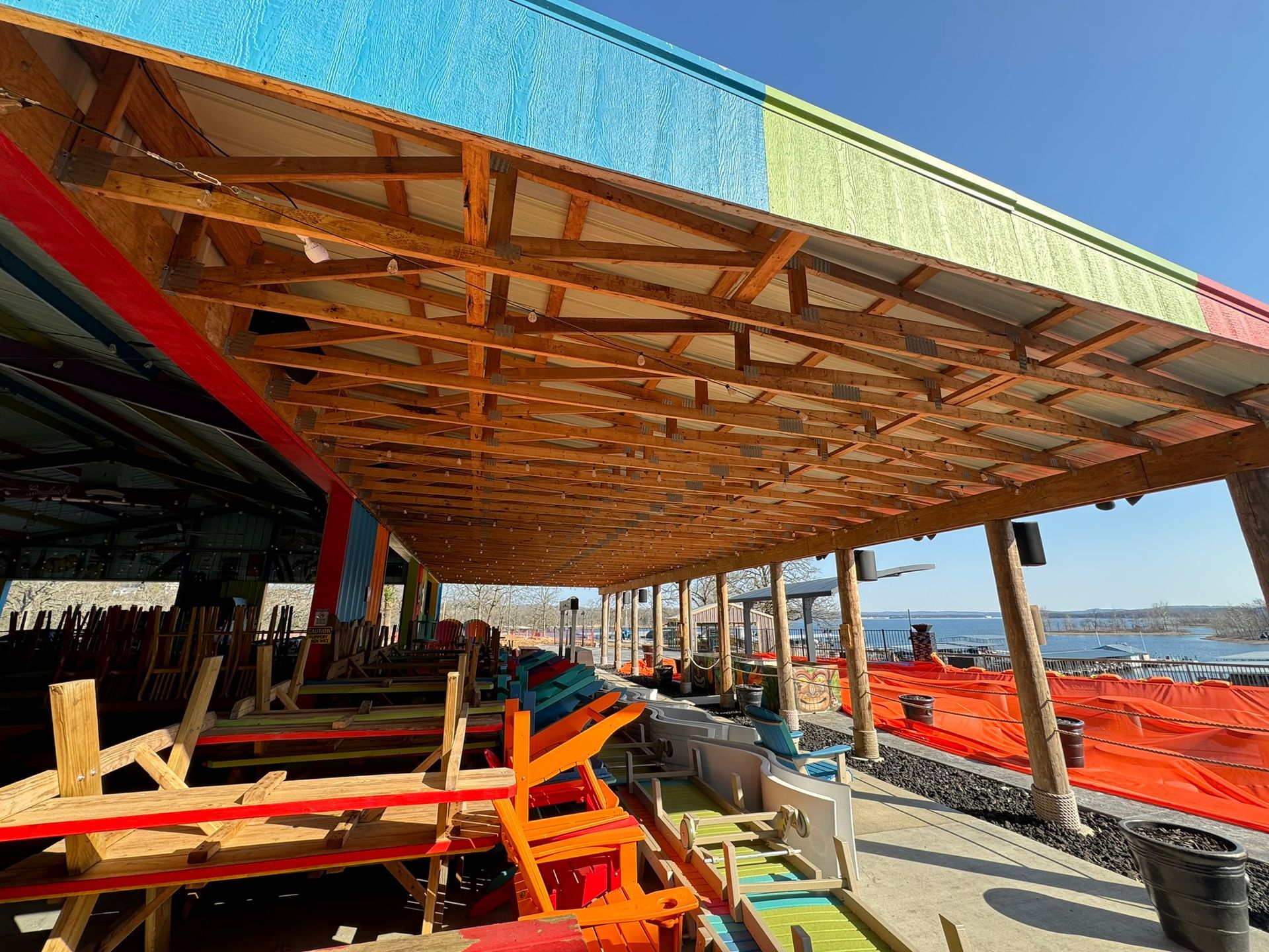 Outdoor construction site with a large wooden roof frame, red beams, and workers in the shade