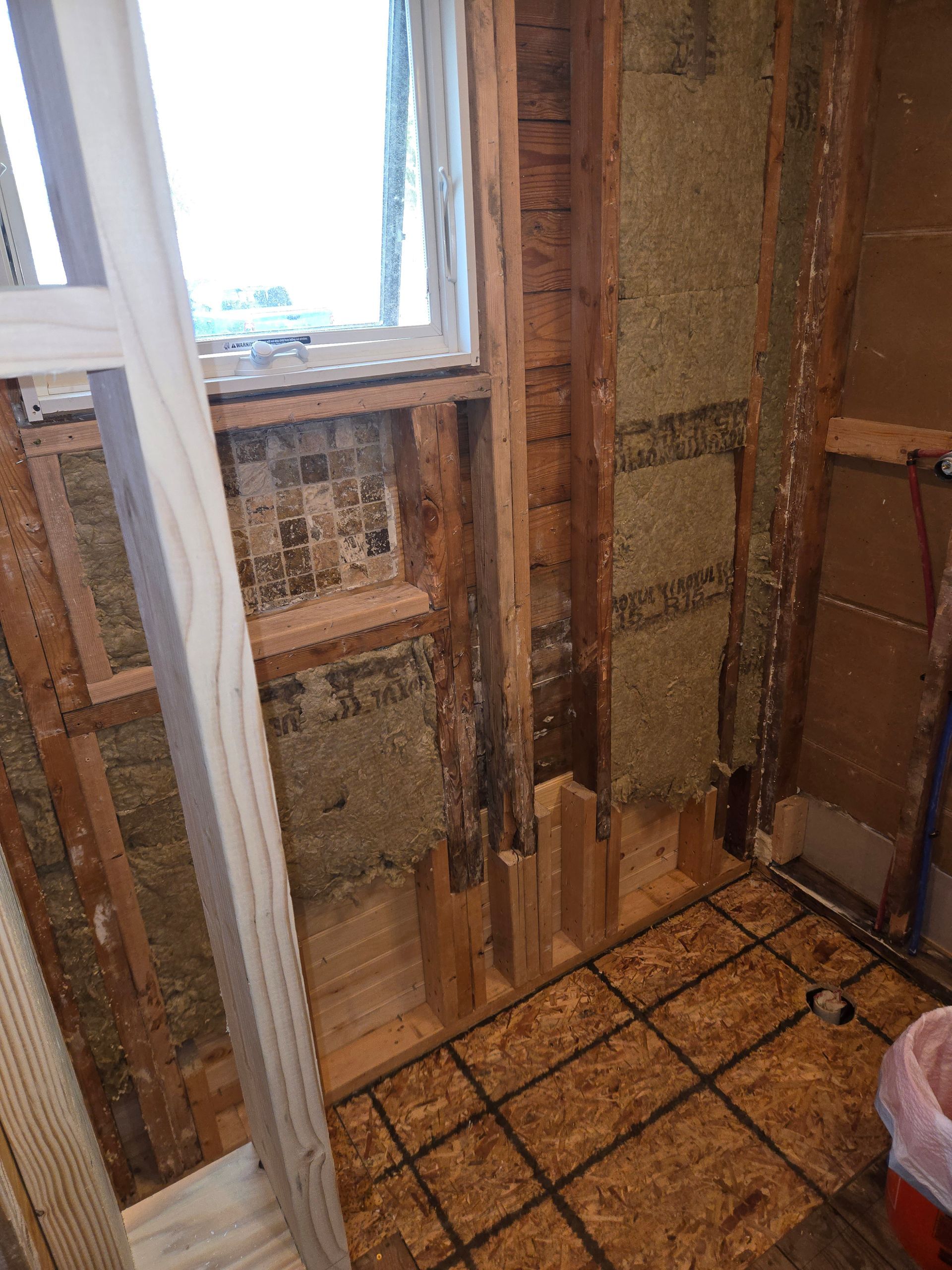 Partially renovated bathroom with exposed wall studs, a window, and a tiled floor under construction