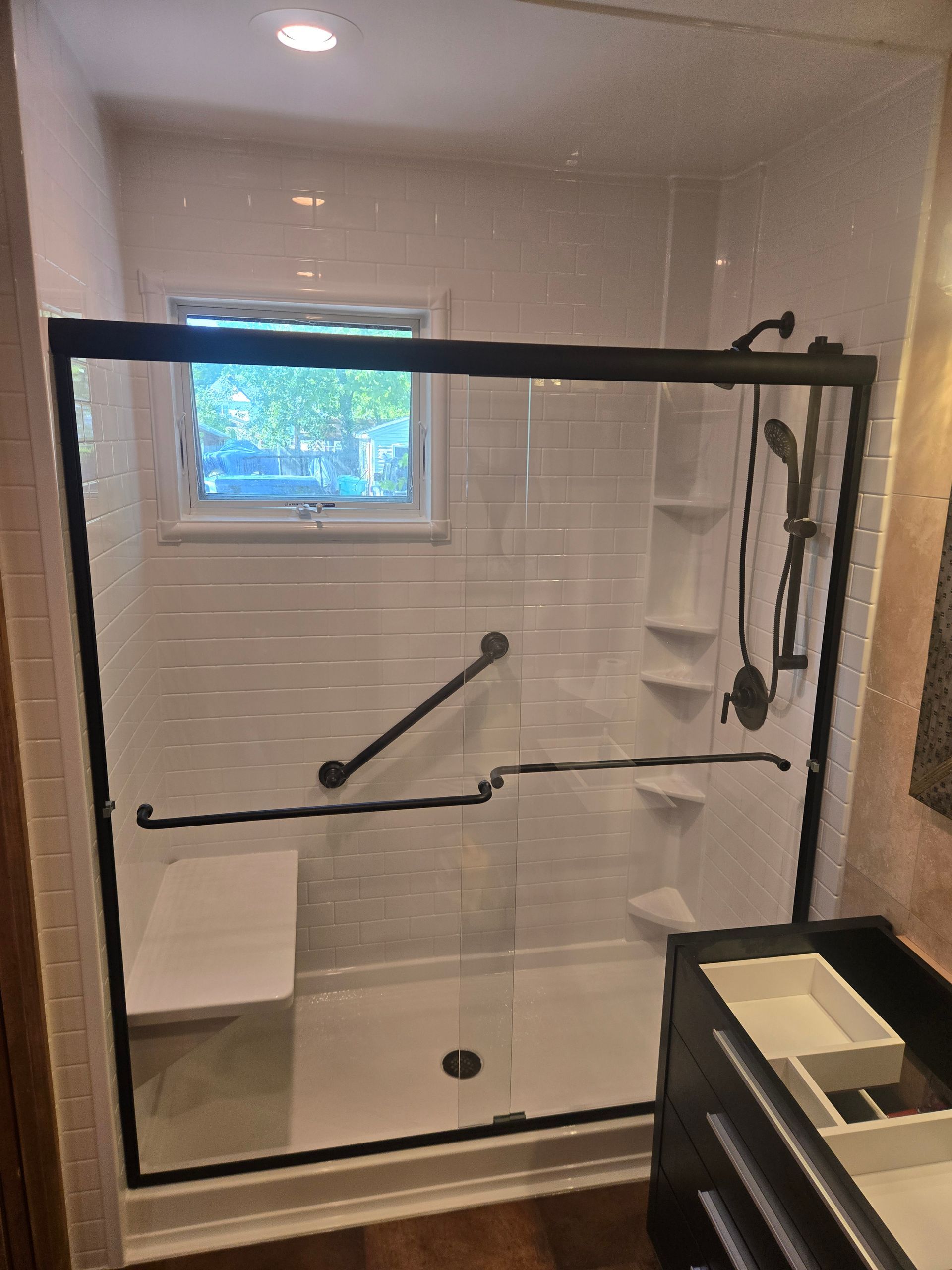 Glass-enclosed walk-in shower with grab bars, built-in bench, and a small window.