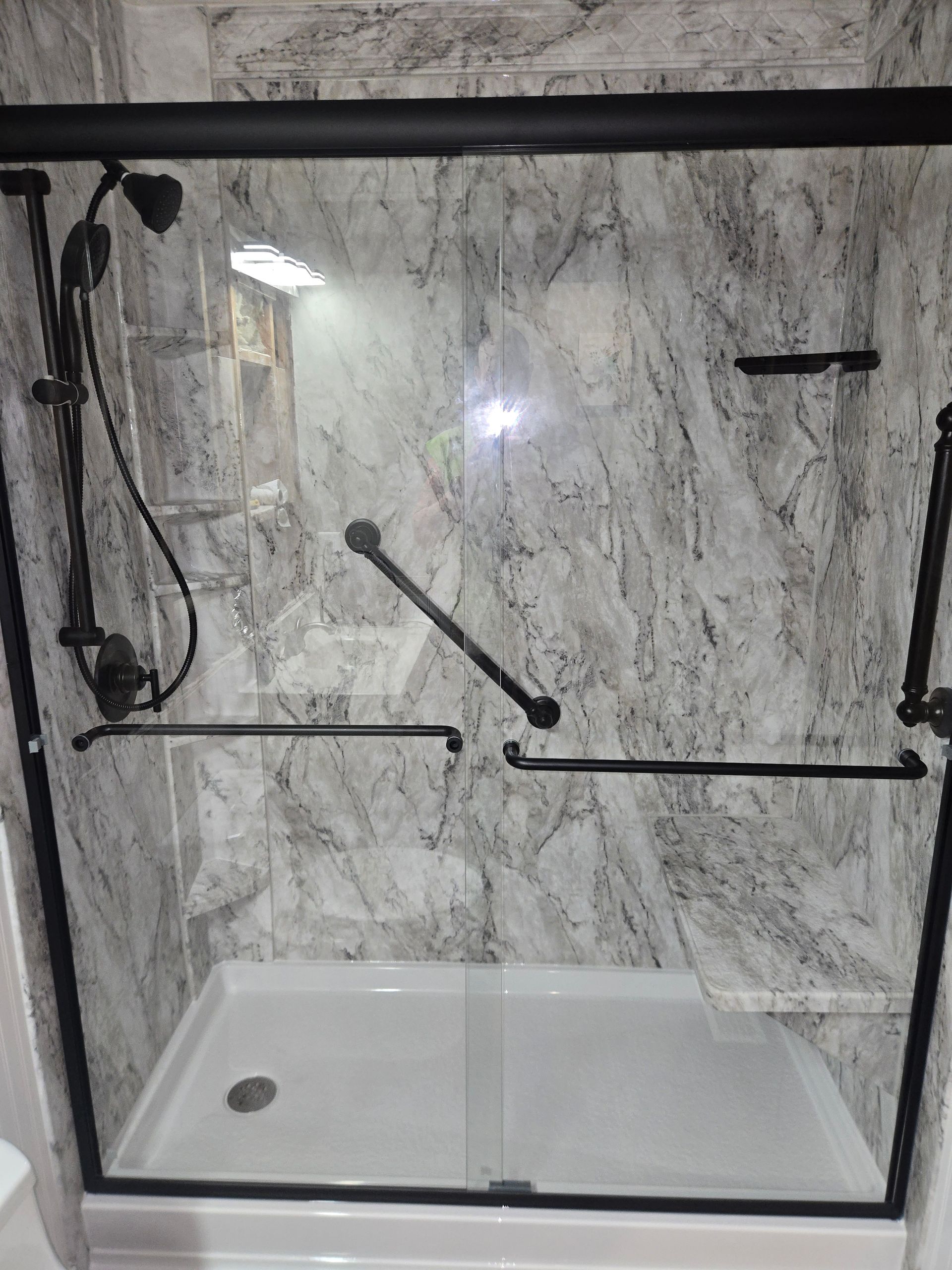 White-tiled shower with black-framed glass doors, handrails, and showerhead.