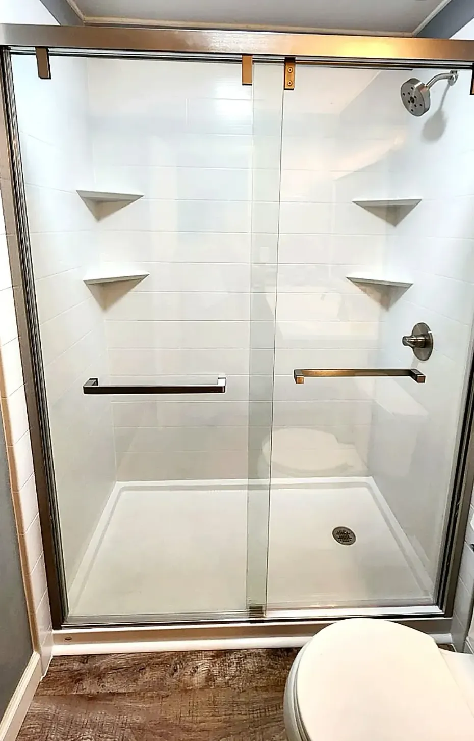 A modern walk-in shower with a sliding glass door, white tiled walls, built-in corner shelves, and a silver shower head.