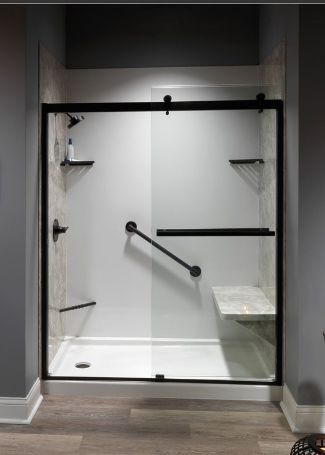 A walk-in shower with a black-framed sliding glass door, white walls, built-in shelving, a marble bench, and a grab bar.