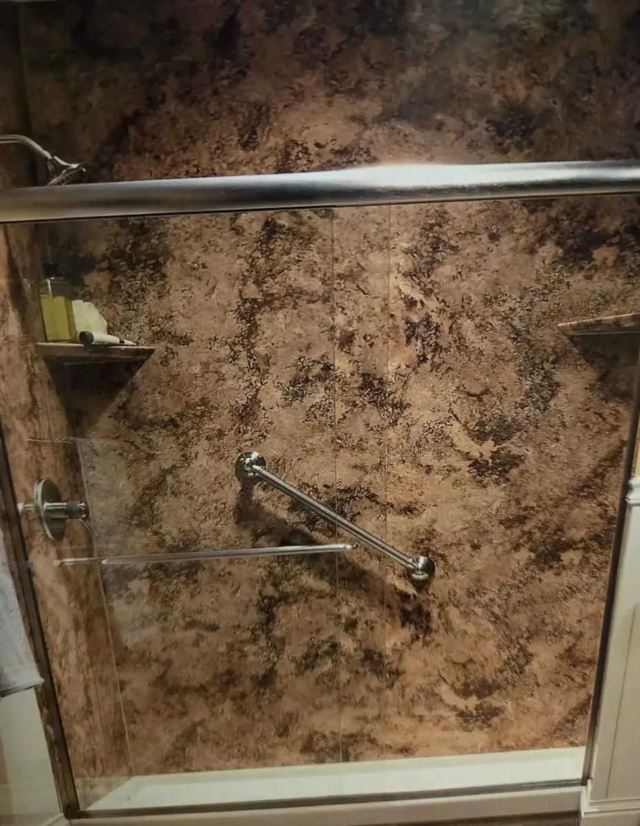 A walk-in shower with textured, brown stone-look walls, a silver grab bar, and a built-in corner shelf.