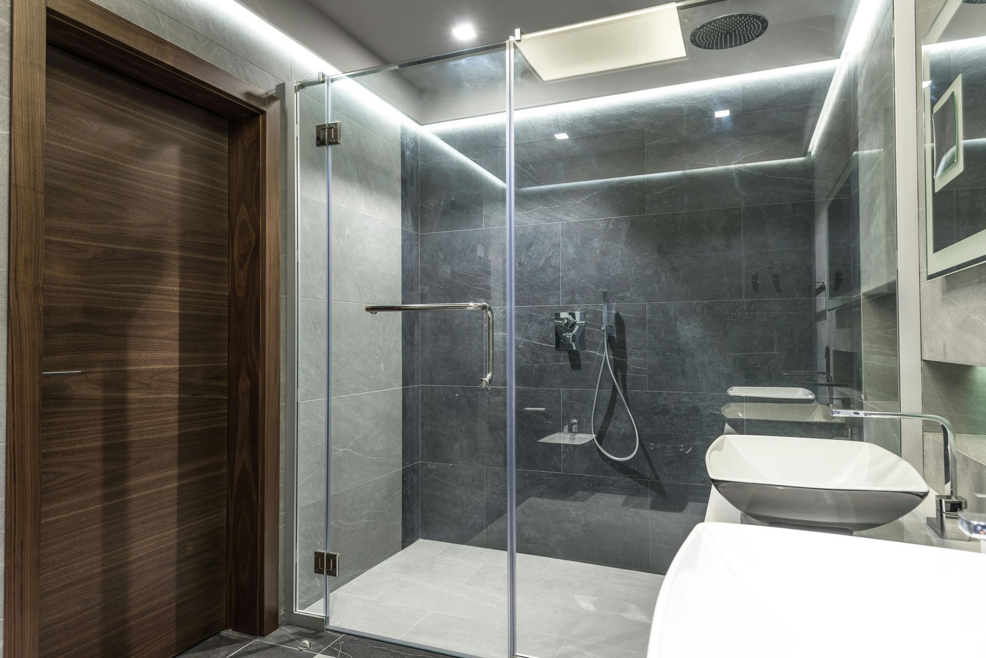 A modern walk-in shower with a sliding glass door, white tiled walls, built-in corner shelves, and a silver shower head.